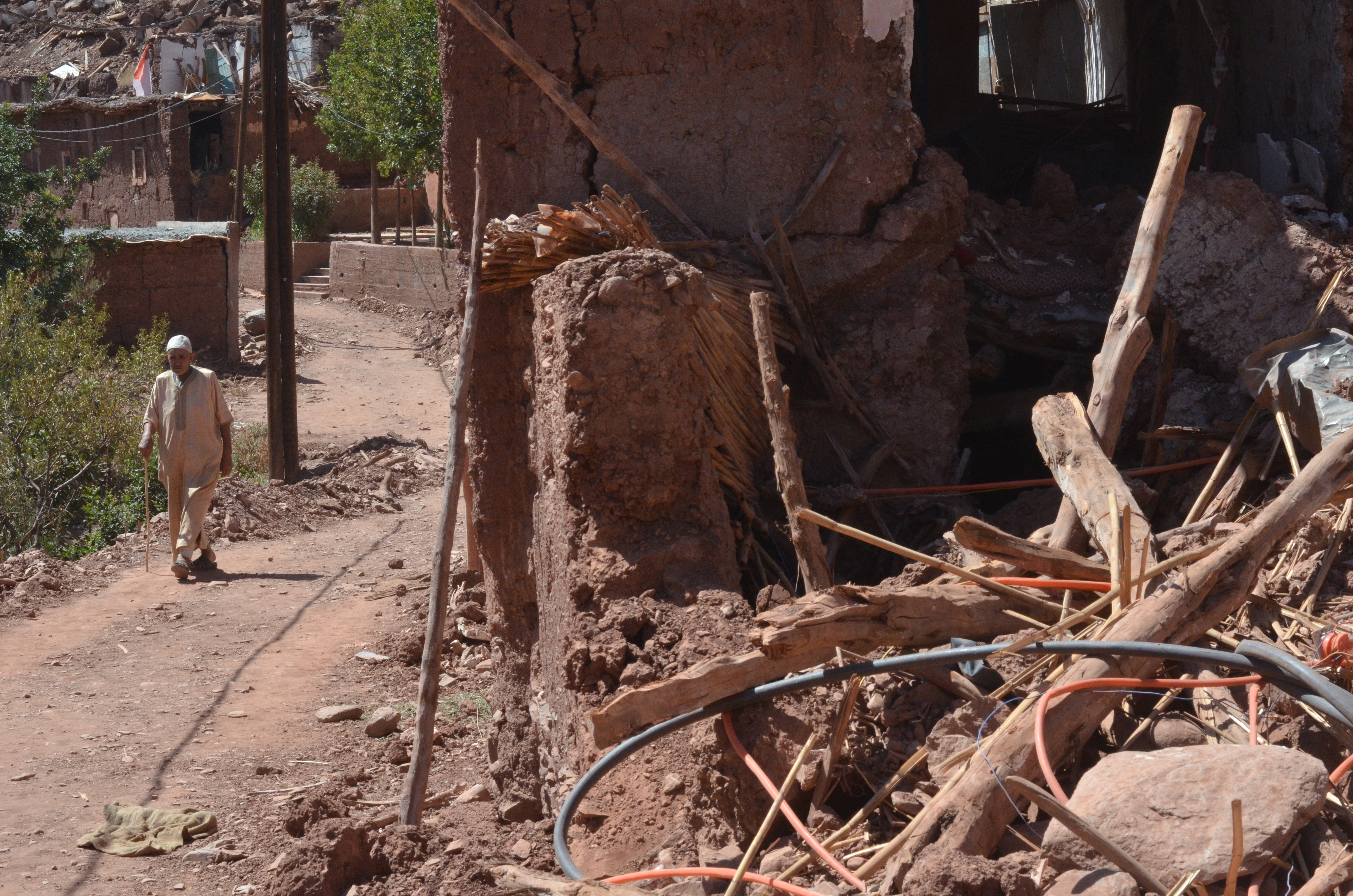 An elderly man walks along a road next to the wreckage of a building.