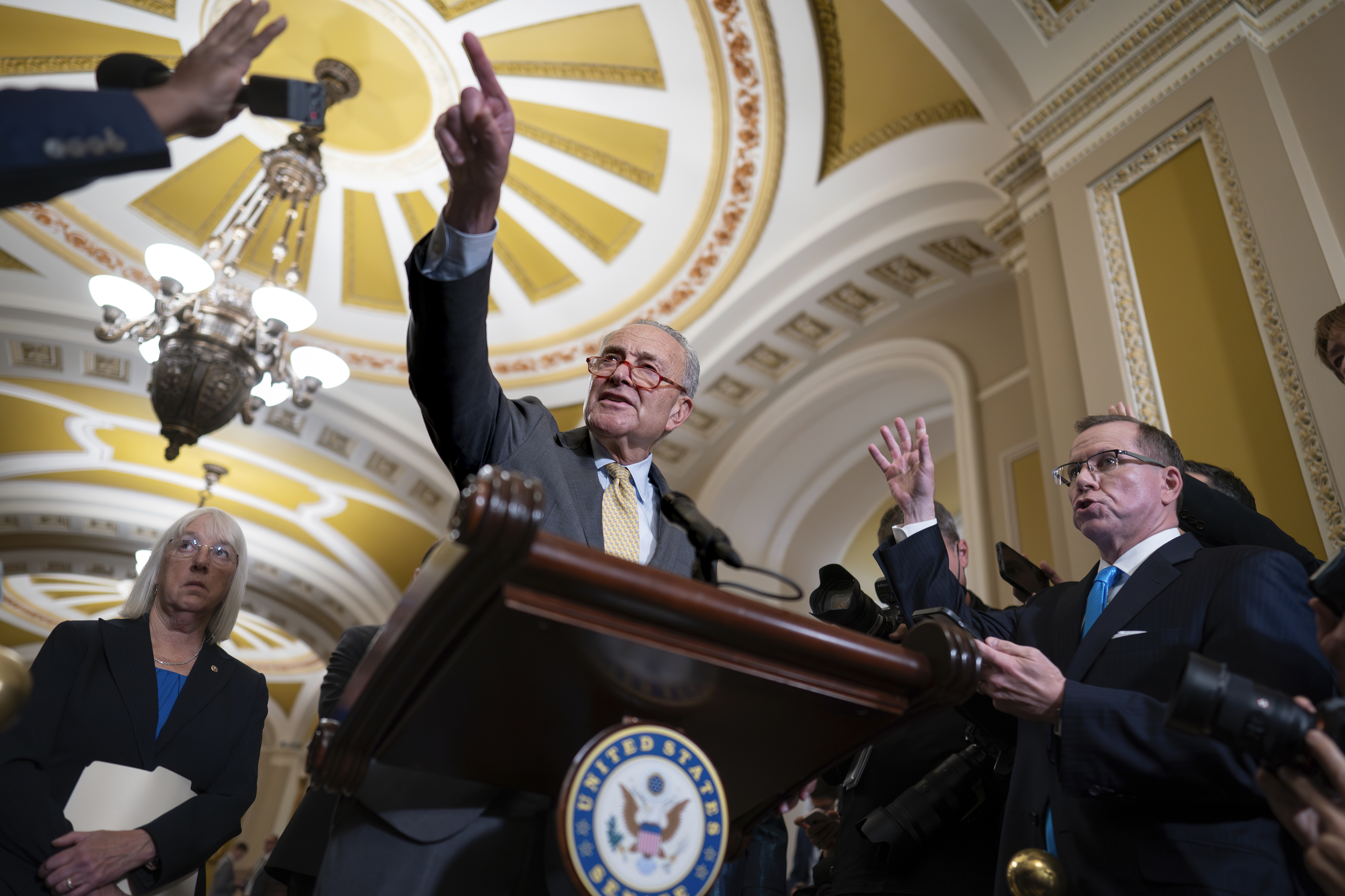 Senate Majority Leader Chuck Schumer, D-N.Y., speaks to reporters after a weekly caucus meeting, at the Capitol in Washington, Tuesday, Sept. 19, 2023. Schumer criticized House Republicans, especially hard-right conservatives, for failing to pass appropriations bills due to GOP infighting. He stands behind a podium, his finger pointed into the crowd, with the gold ceilings of the Capitol behind him.