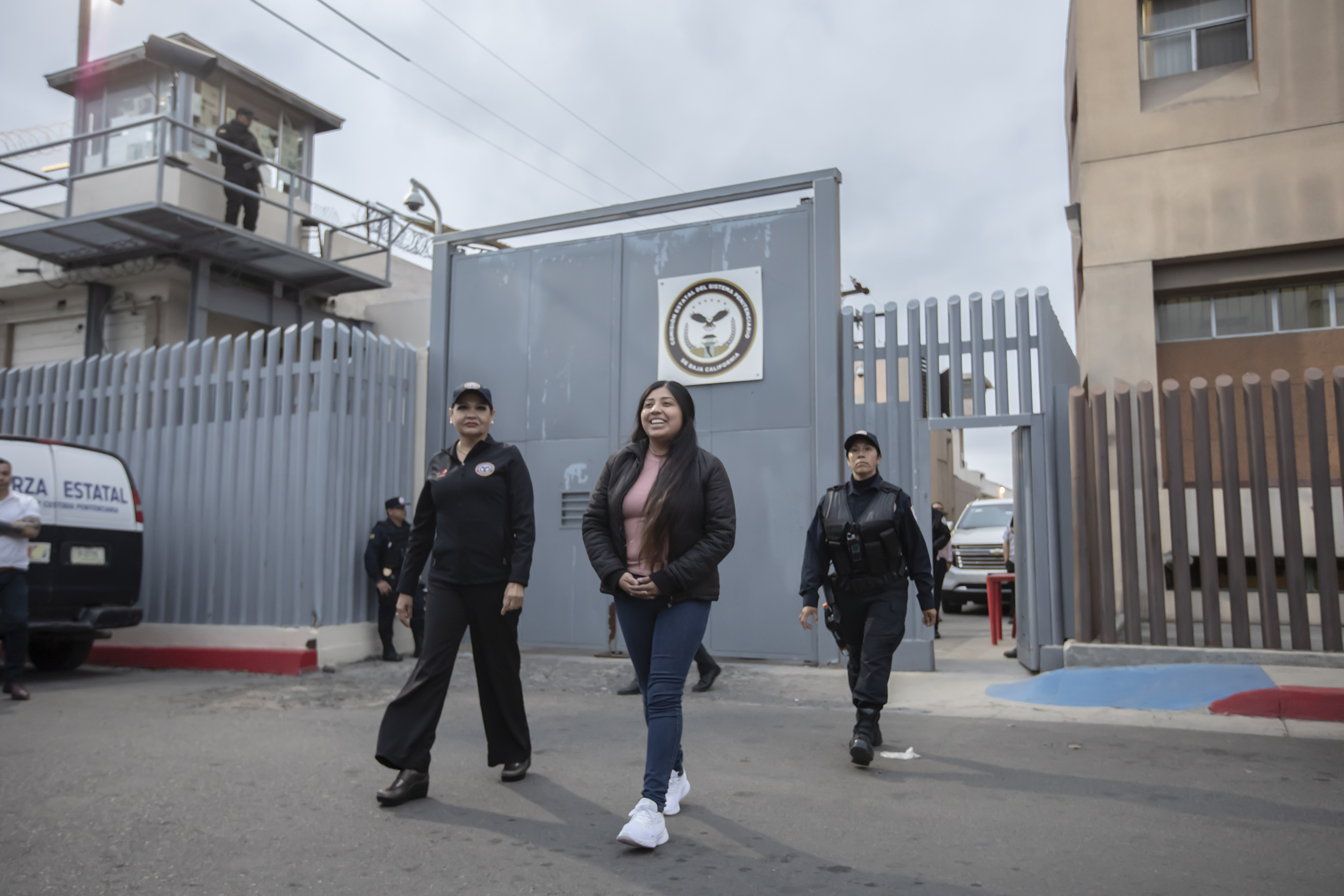 Alina Narciso walks with two police officers away from the gate of La Mesa prison and onto the street.