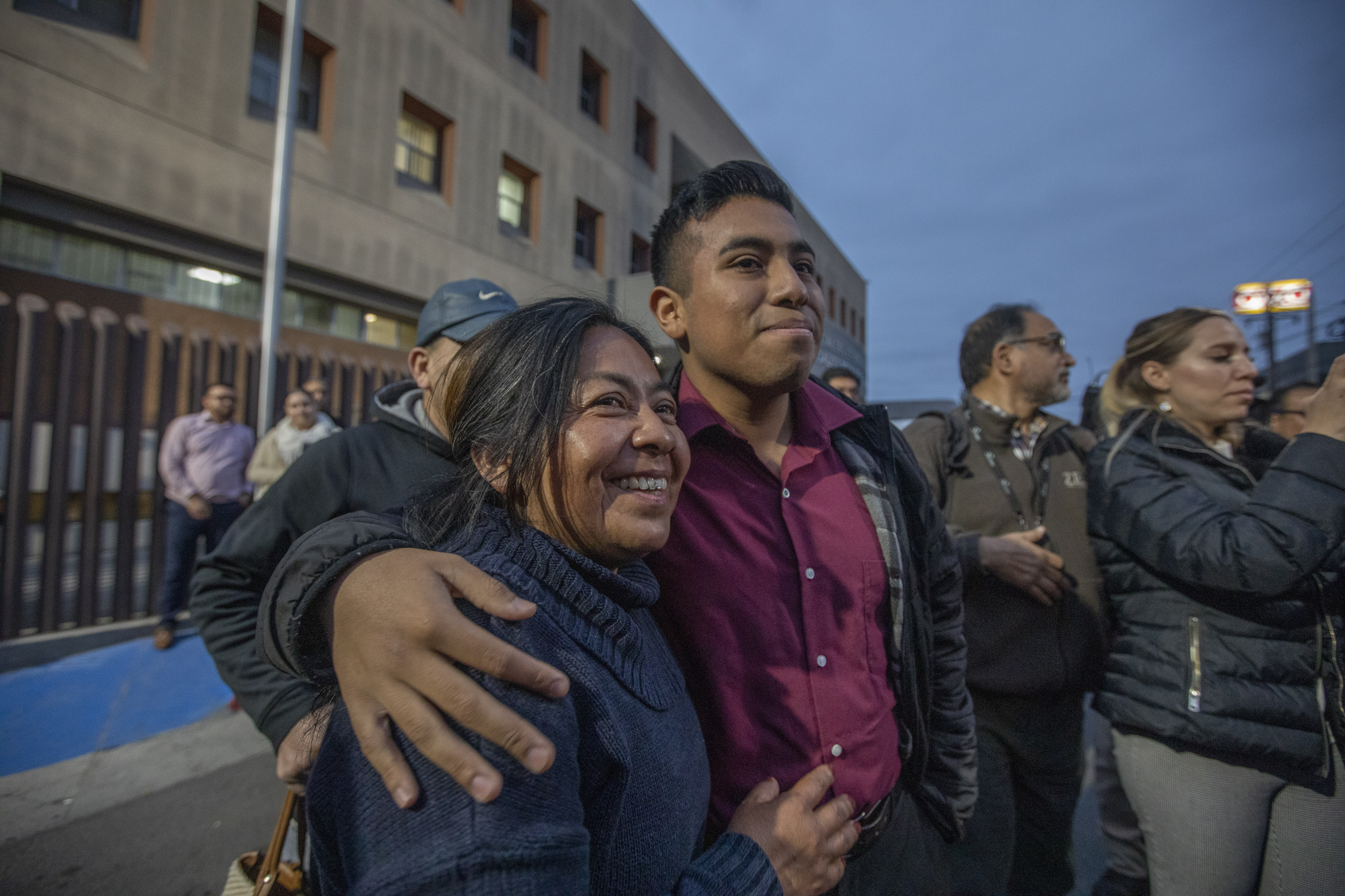 A man wraps his arm around an older female family member, who smiles with anticipation. The photo depicts members of Alina Narciso's family waiting for her release outside the La Mesa prison in Tijuana in May 2023.