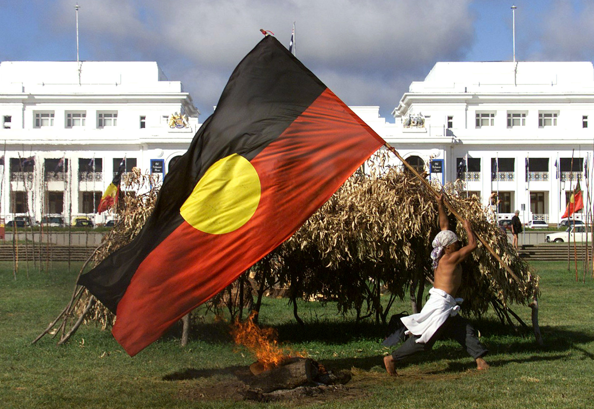 An Aboriginal protester runs past a fire and make-shift shelter with an Aboriginal flag outside the old parliament House building in Canberra