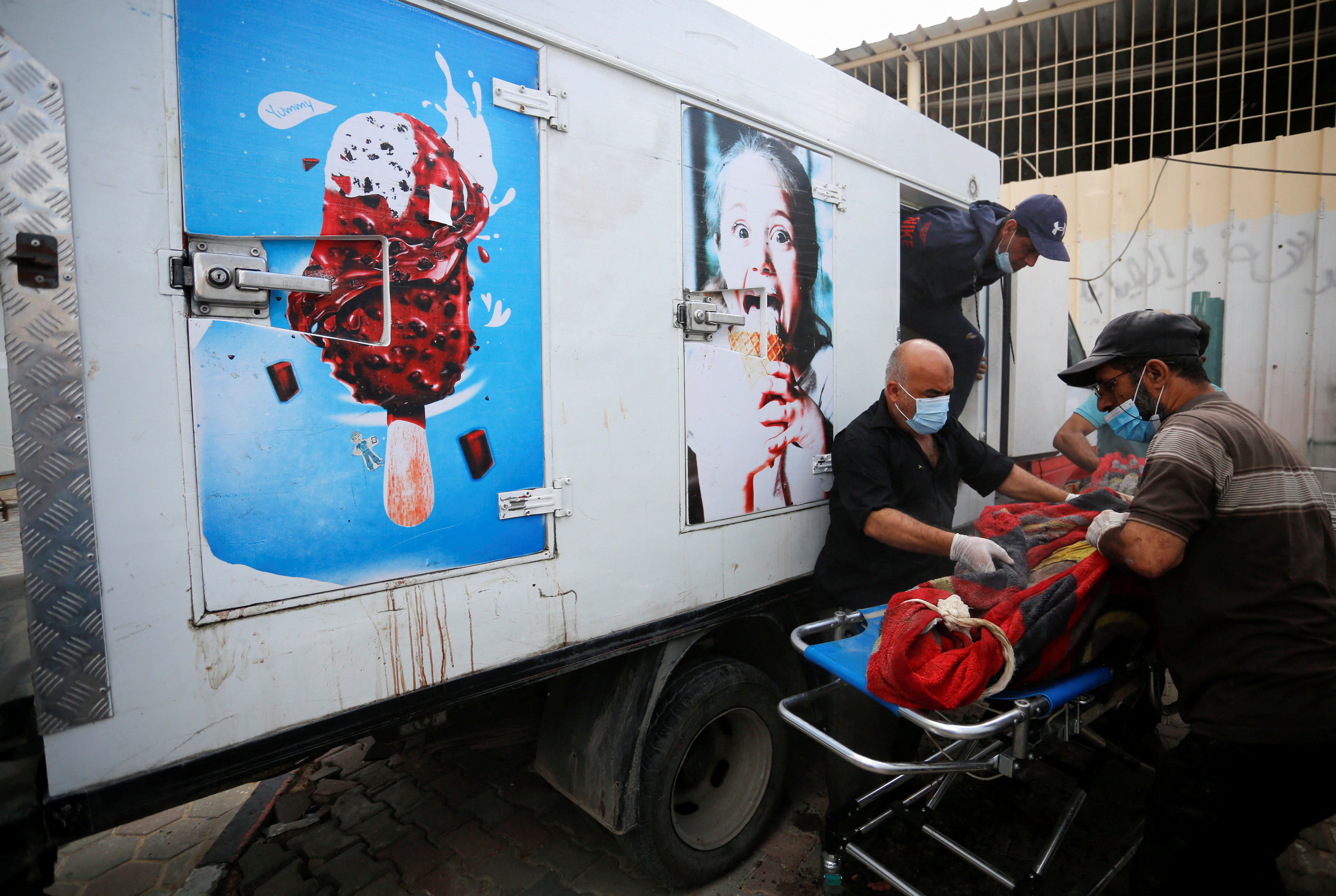People move the body of a Palestinian, who was killed in Israeli strikes, from an ice cream truck where it was kept, as the hospital morgues are packed