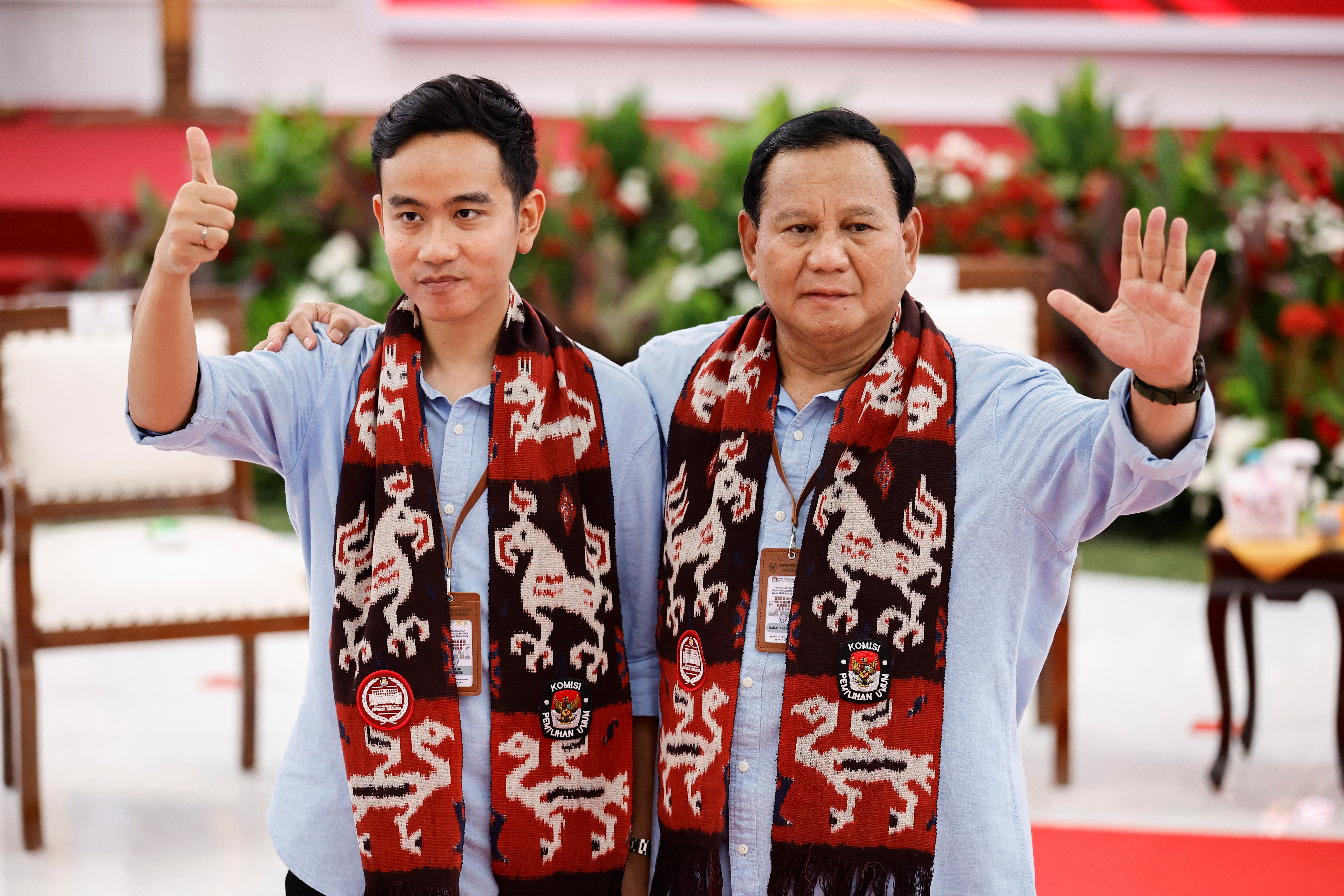 Prabowo and Gibran ahead of the registration of their candidacy They are wearing blue shirts and have scarves around their necks. They are waving.