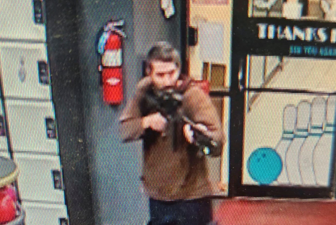 The photo of the suspect released by police. He is wearing a brown shirt and jeans an holding the rifle to his shoulder in a shooting position.