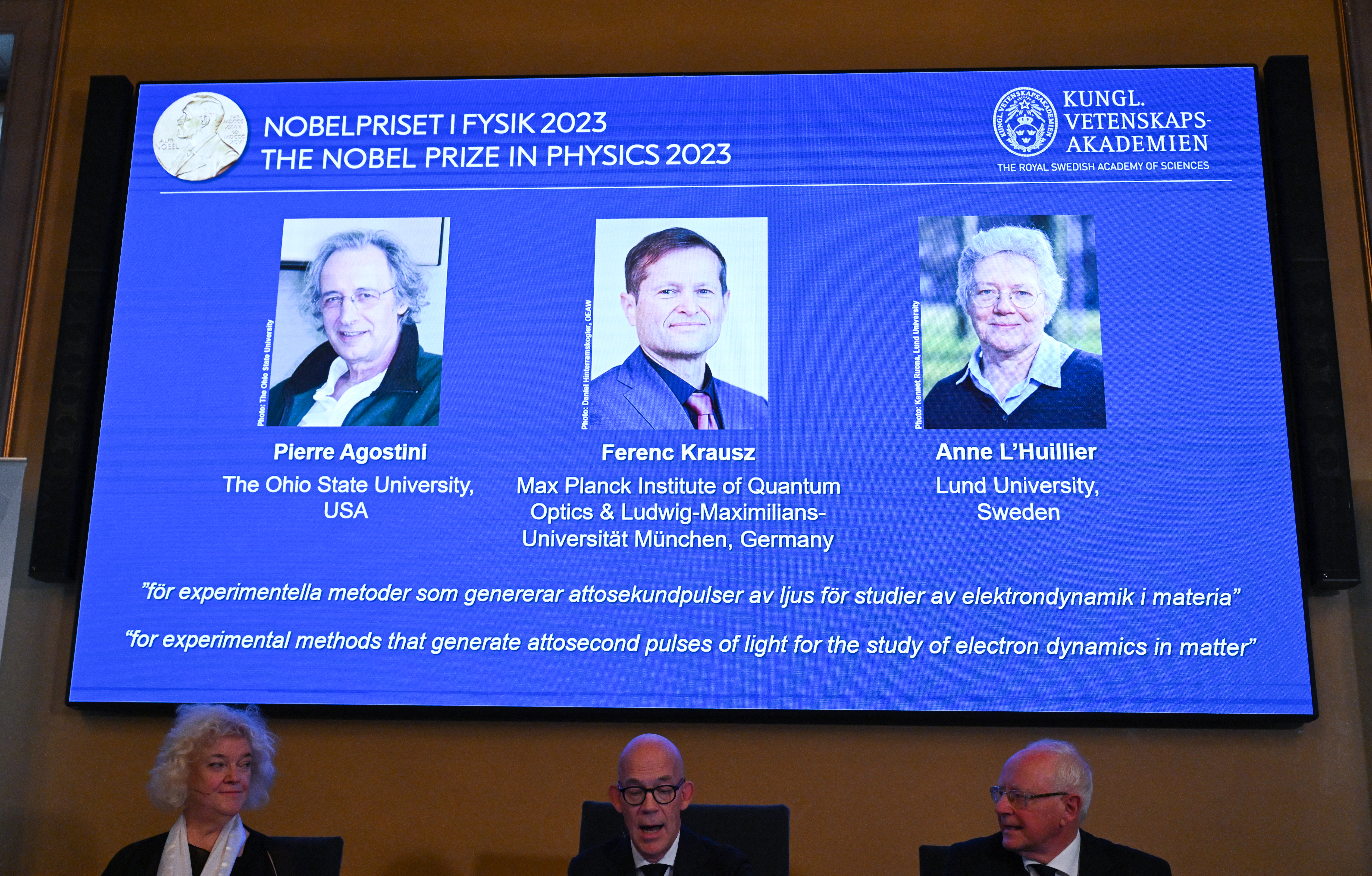 (L-R) US-based physicist Pierre Agostini, Hungarian-Austrian physicist and French physicist Anne LHuillier appear on the screen as member of the Royal Swedish Academy of Sciences Chair of the Nobel Committee for Physics Eva Olsson, Secretary General of the Royal Swedish Academy of Sciences and Member of the Nobel Committee For Physics speak to the media during the announcement of the winners of the 2023 Nobel Prize in Physics at Royal Swedish Academy of Sciences in Stockholm on October 3, 2023.