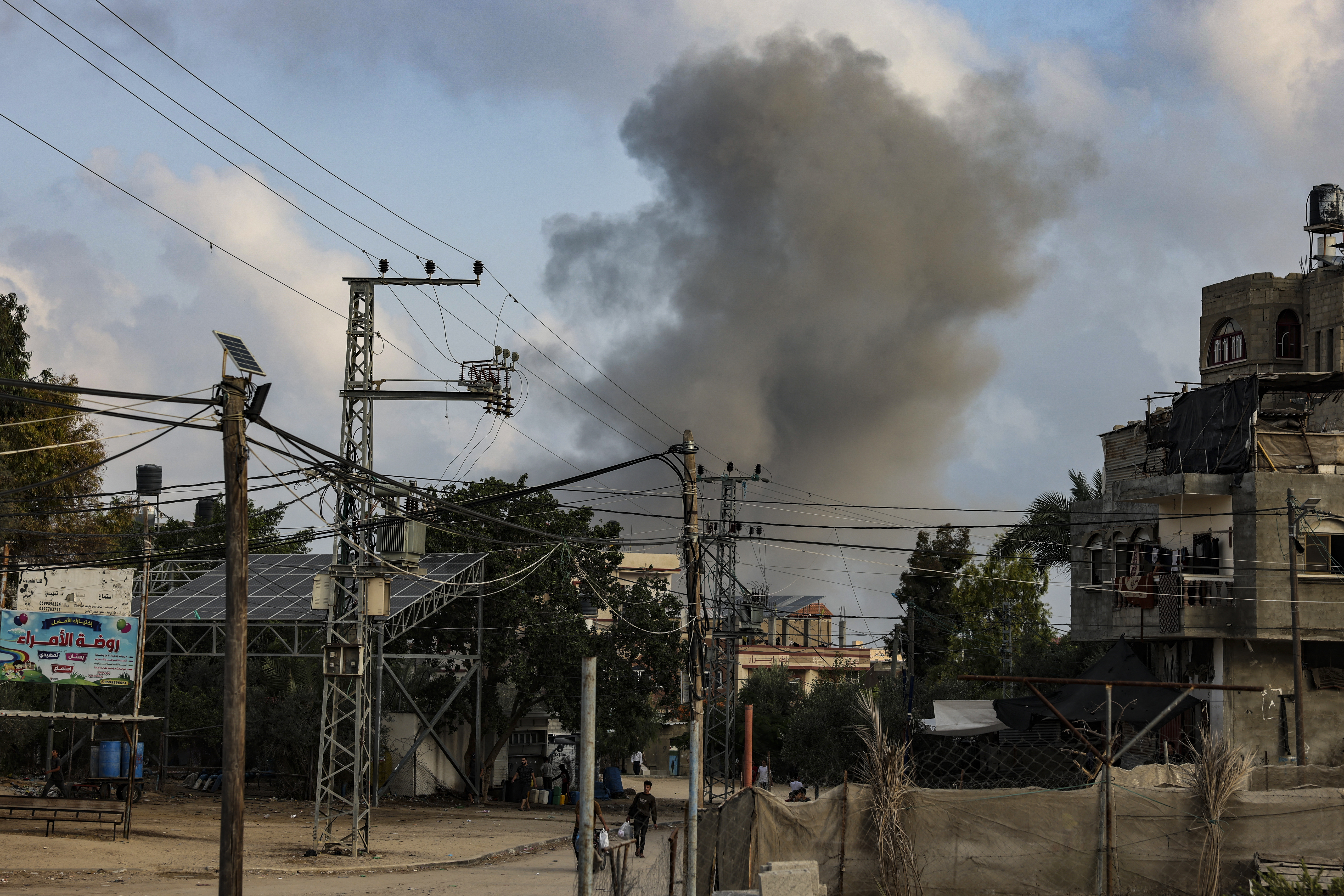 A young man transports a bag of food as smoke rises from buildings behind him during an Israeli strike in Rafah