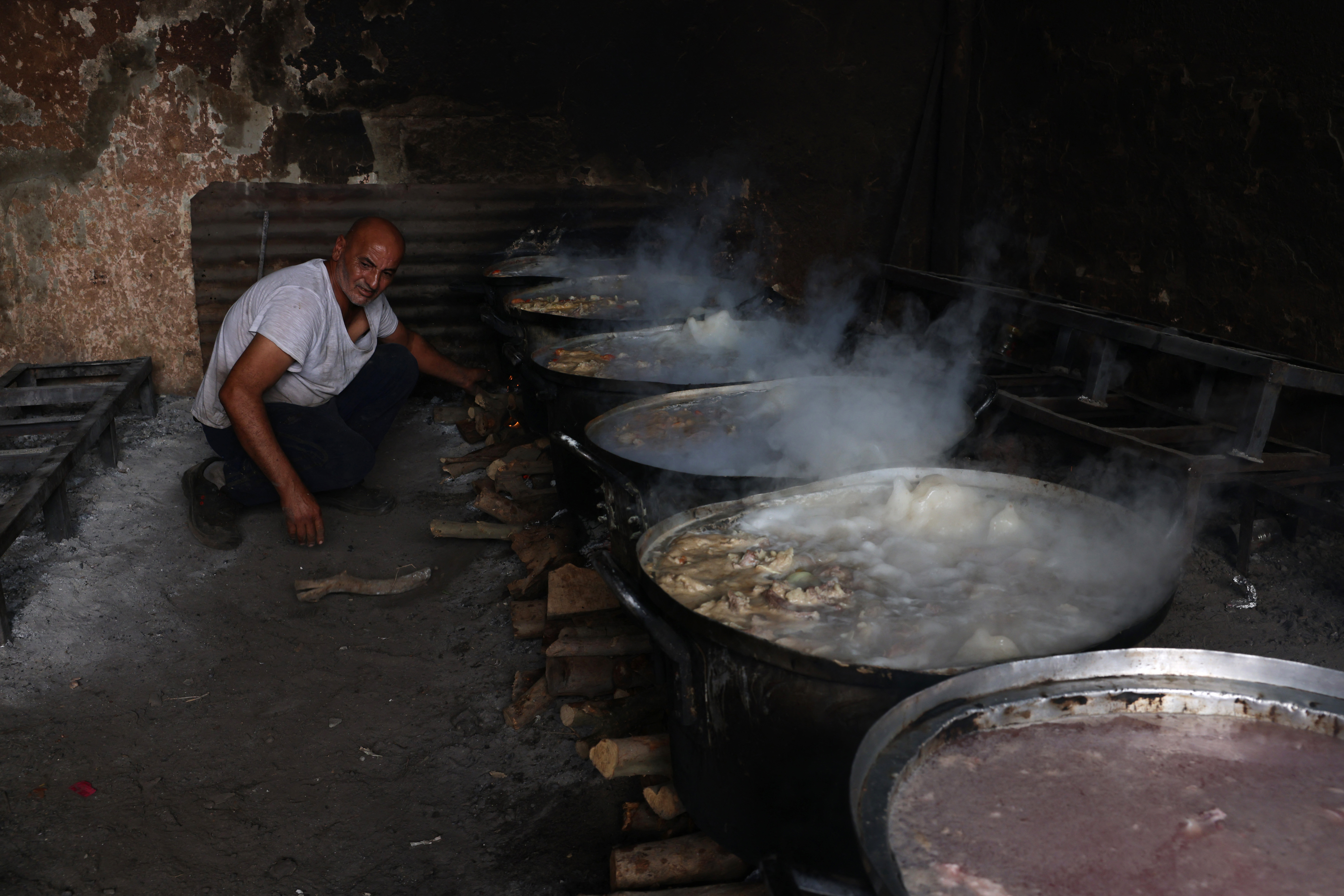 A Palestinian man adds fire wood under large pots simmering of food which will be distributed to displaced families following Israel's call for more than 1 million residents in northern Gaza to move south, in Rafah