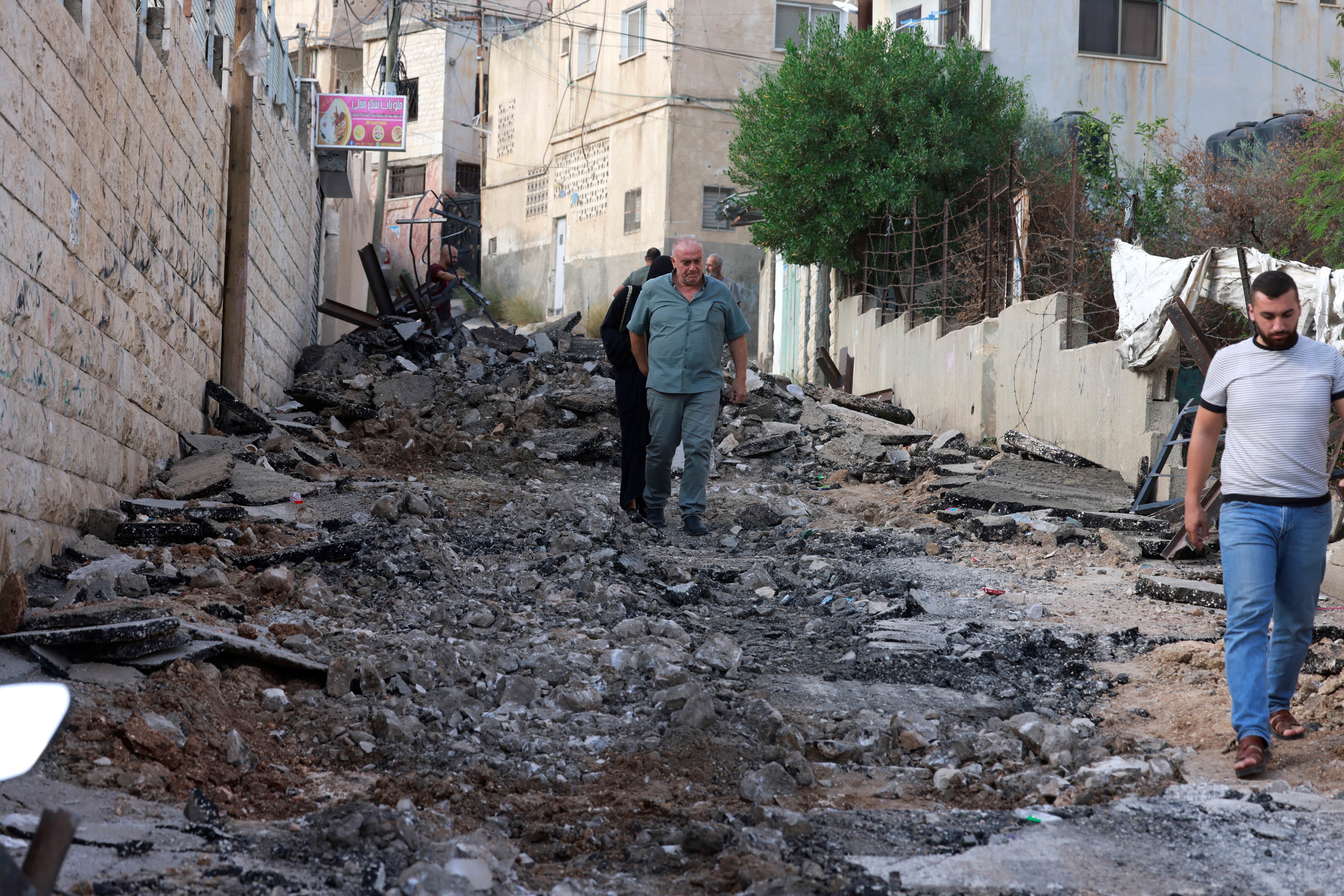 Palestinians stand on a damaged street, following an Israeli raid in Jenin,