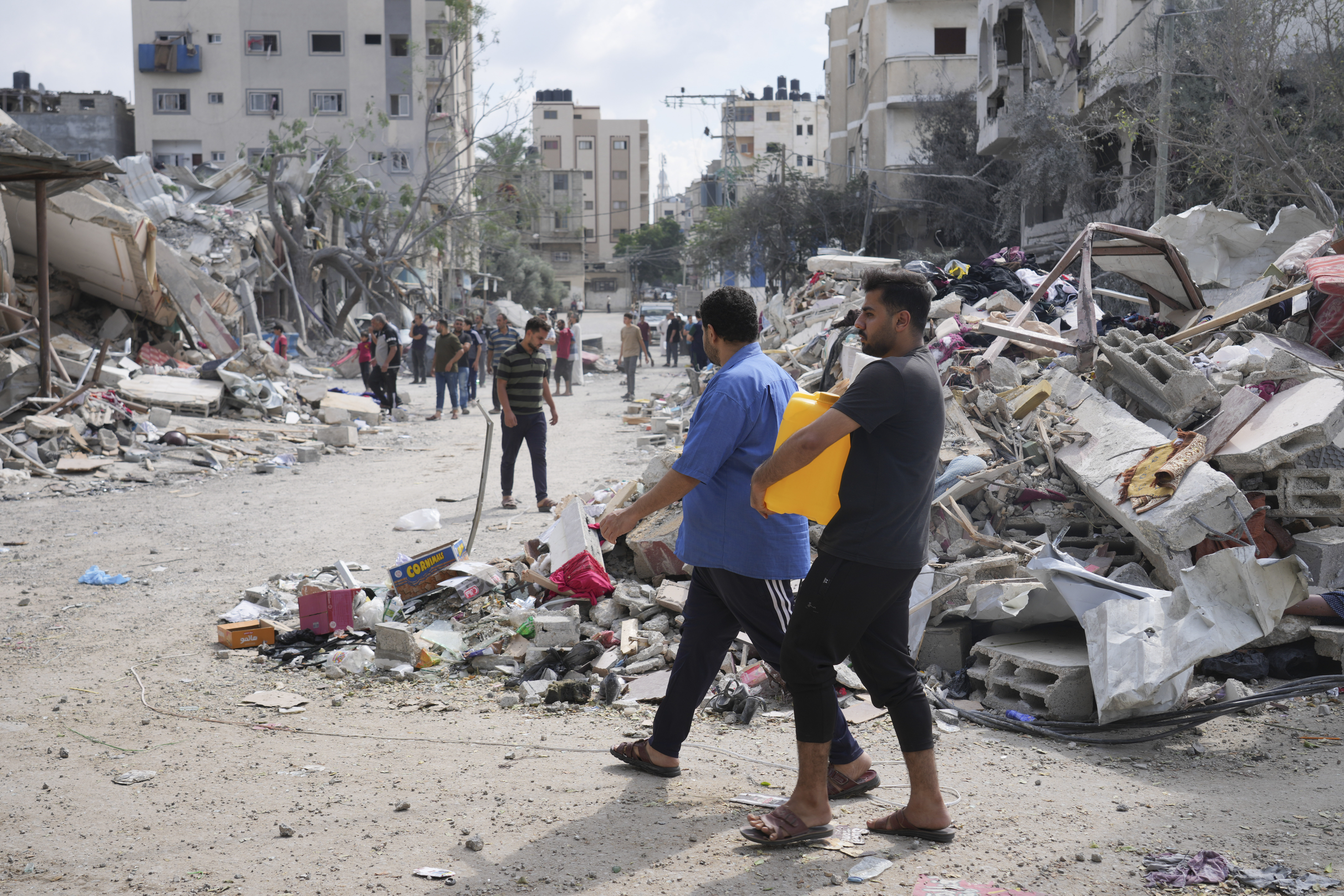 A Palestinian carries a water canister by the buildings destroyed in an Israeli airstrike in Nuseirat camp in the central Gaza Strip, Monday, Oct. 16, 2023.