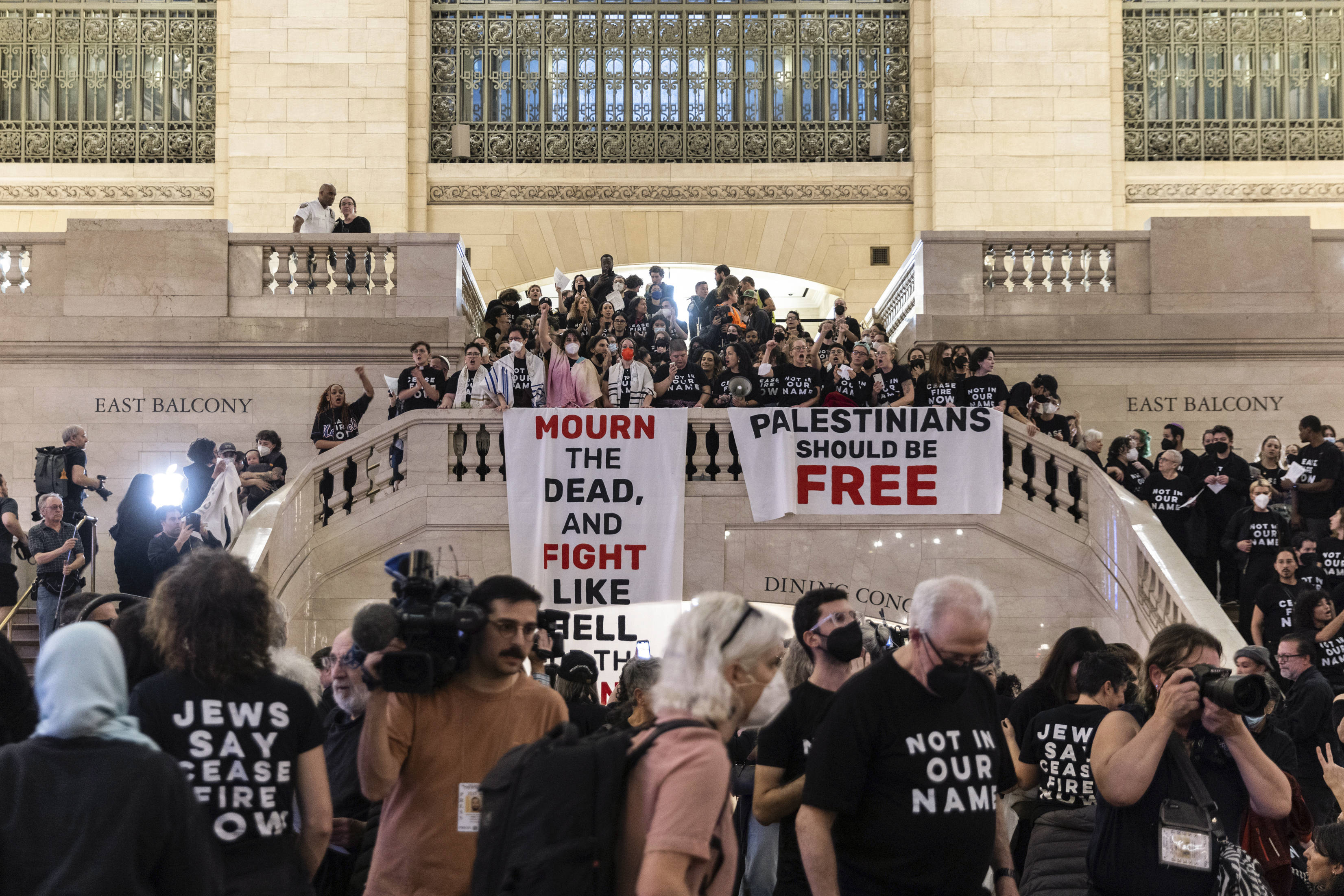 Protesters gathered on the concourse of New York's Grand Central Station. They are wearing black and hanging a banner reading 'Palestinians must be free' from the top of the staircase