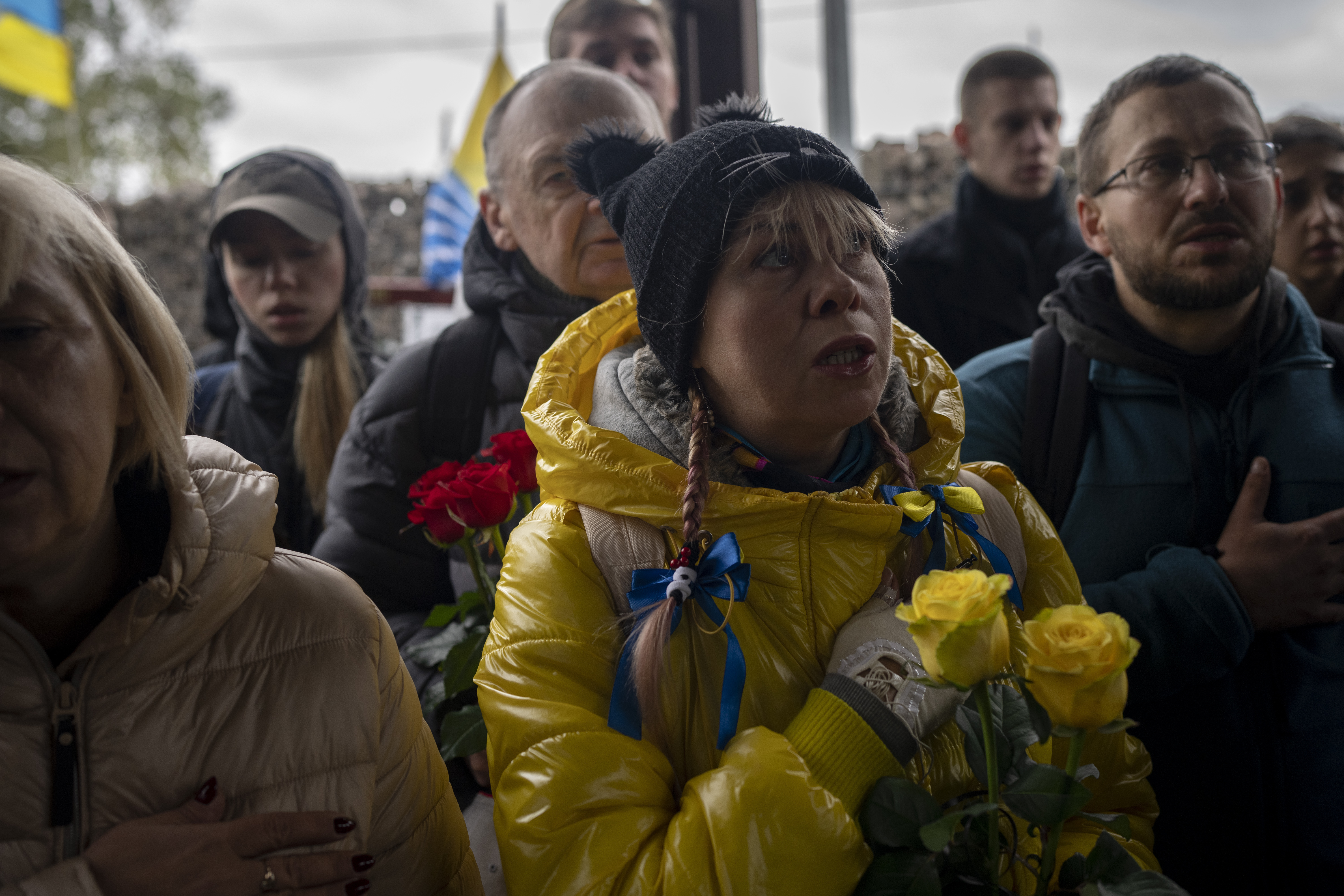 Mourners sing the Ukrainian national anthem. They are at a funeral for a soldier killed in Mariupol. They have their hands on their hearts.