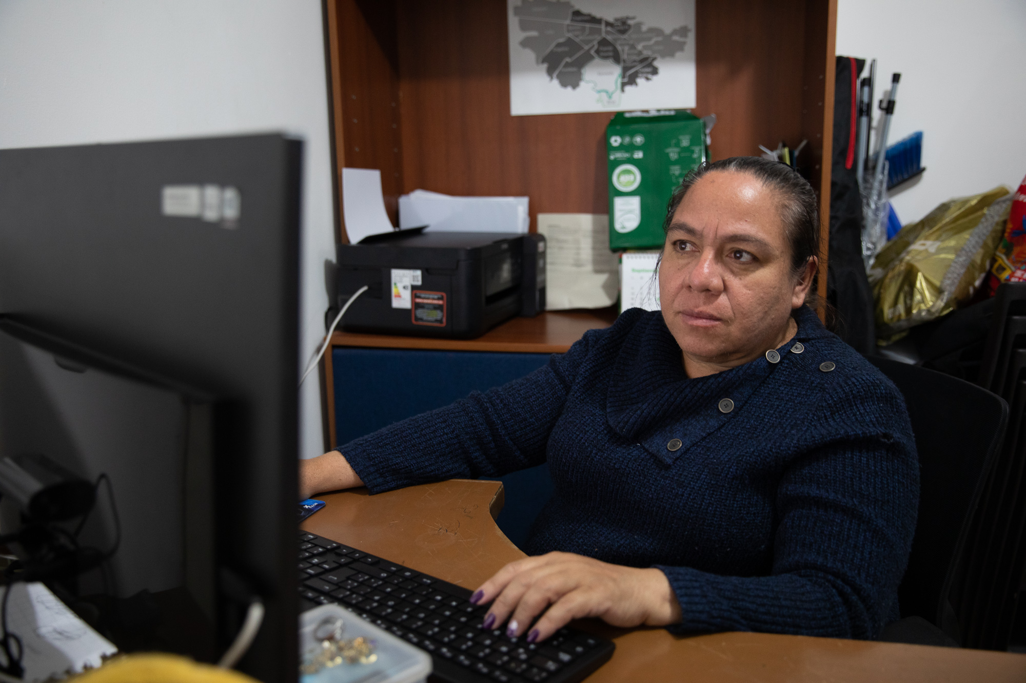 Gisela Serrano sits at a wooden desk, a computer in front of her and her hand resting on its keyboard.