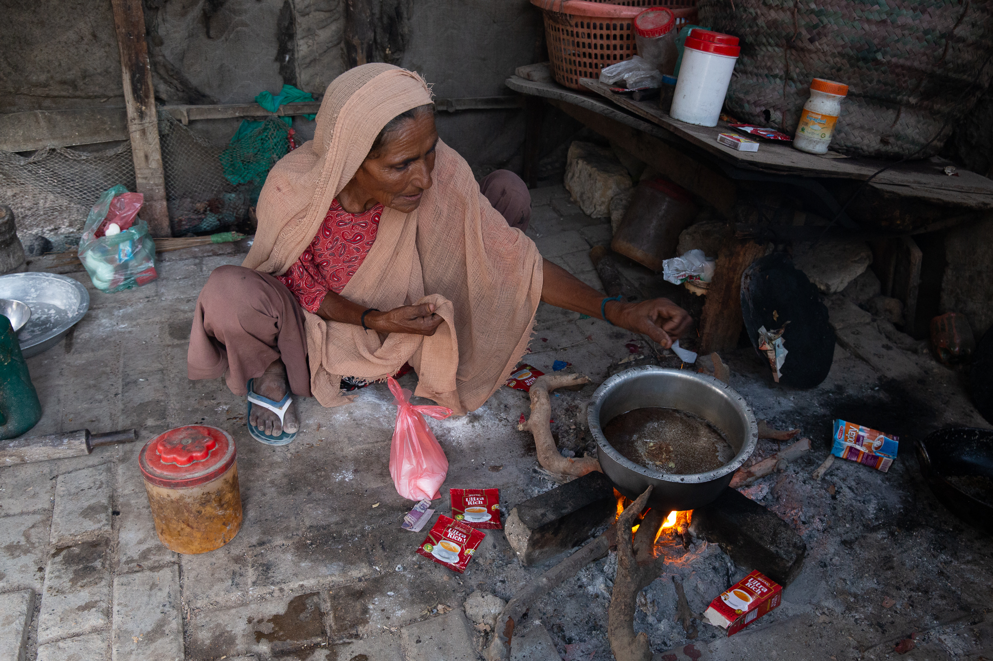 A photo of a woman cooking something using a campfire and a metal pot.