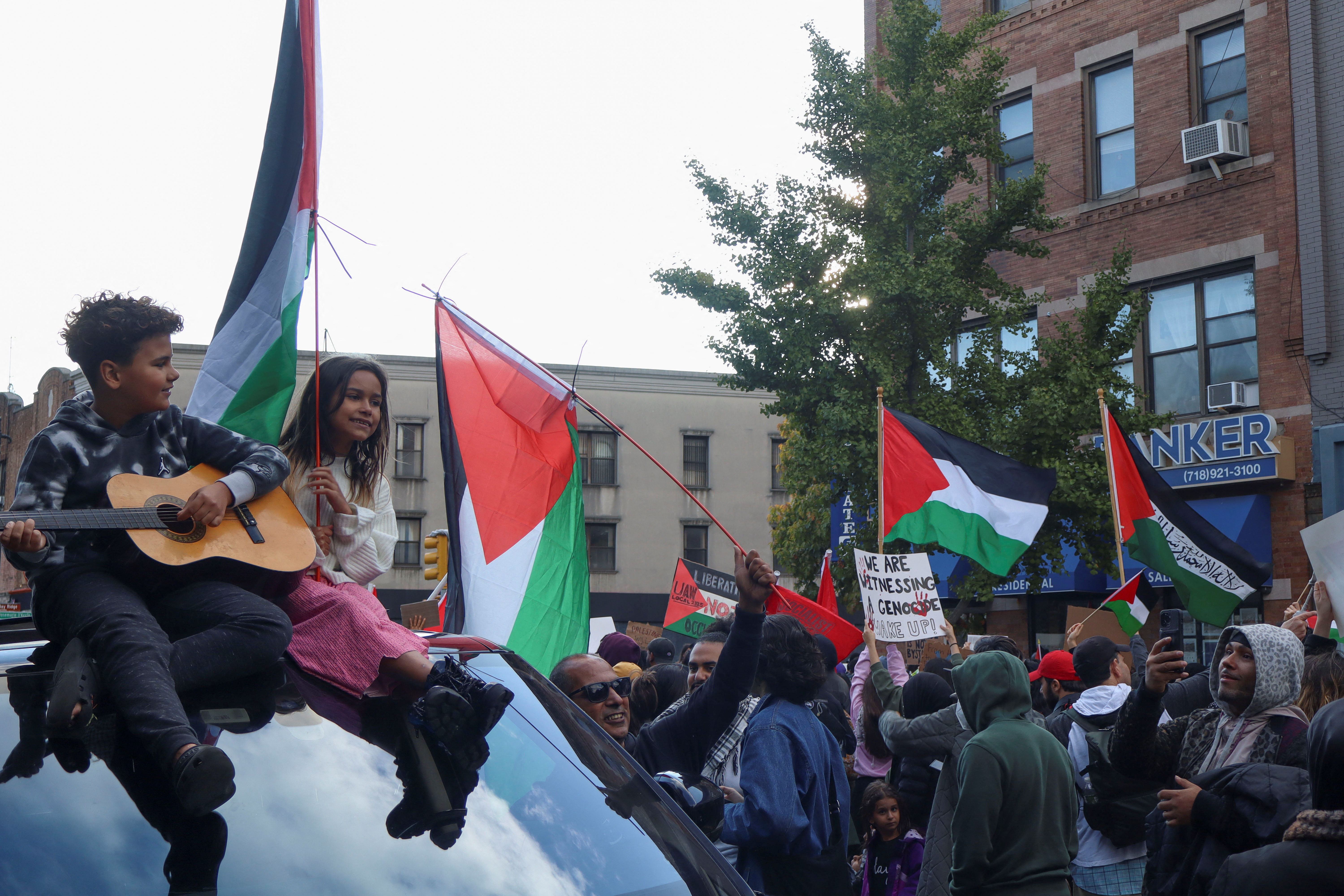 Young children sit on a car and sing "Free Palestine" in New York