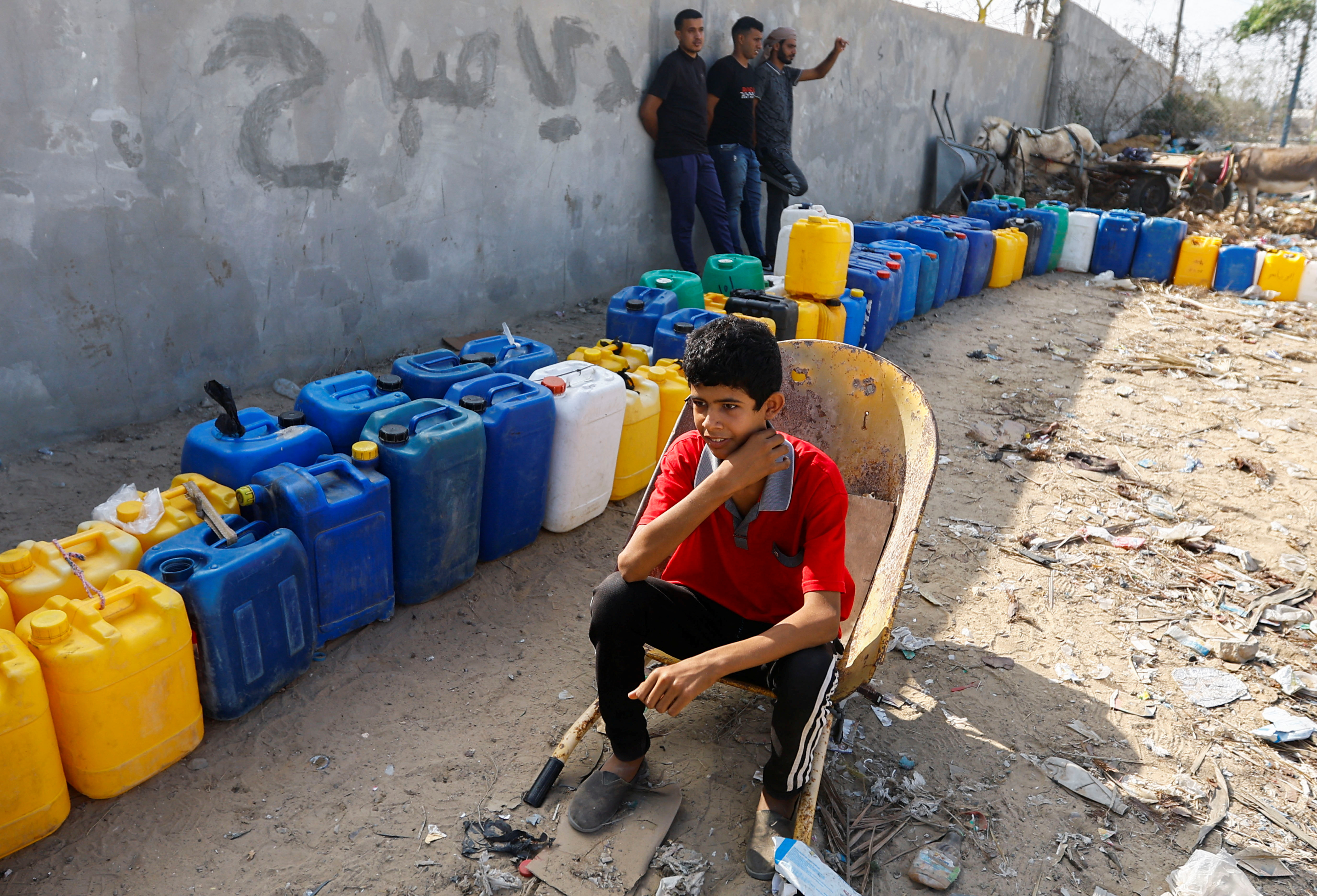 A child sits next to containers, as Palestinians collect water, amid a lack of clean and drinking water, as the conflict between Israel and Palestinian Islamist group Hamas continues, in Rafah, in the southern Gaza Strip