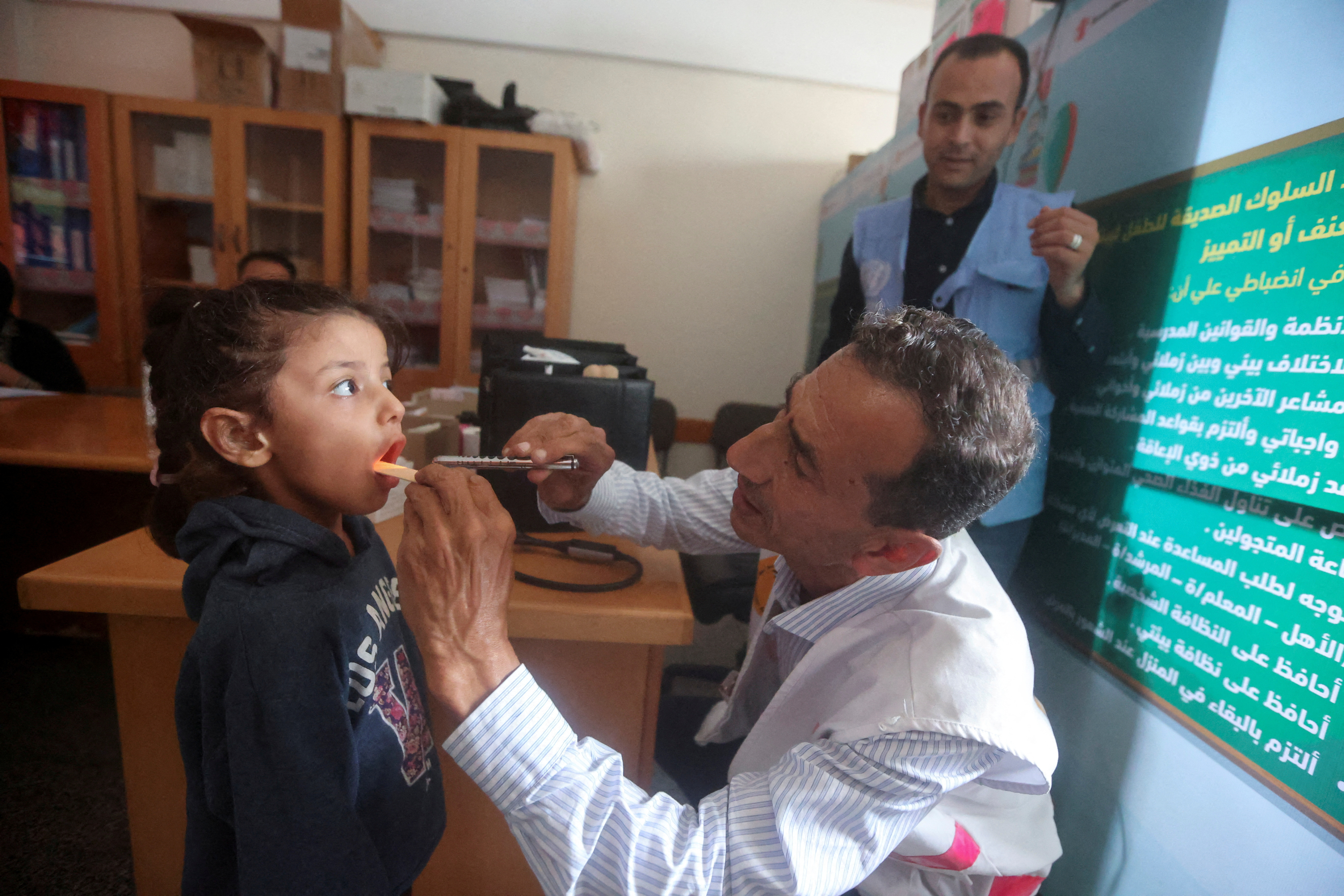 FILE PHOTO: Palestinian doctor Hassan Zain al Din, who travels on his bicycle from one makeshift shelter to another to provide treatment and medication to displaced patients, checks a girl at a school turned into a shelter, amid fuel shortages, as the conflict between Hamas and Israel continues, in Deir al-Balah, in the central Gaza Strip