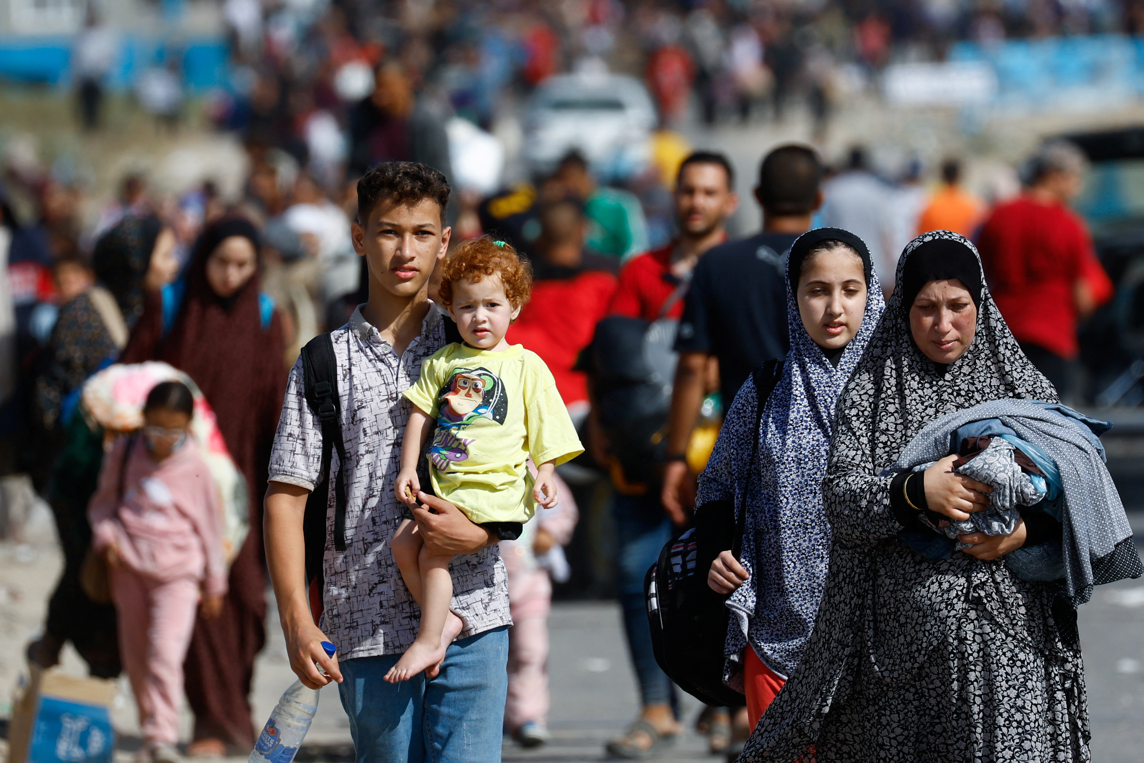 A boy carries a child while Palestinians fleeing north Gaza move southward as Israeli tanks roll deeper into the enclave, amid the ongoing conflict between Israel and Hamas, in the central Gaza Strip November 10, 2023. [Reuters/Ibraheem Abu Mustafa]