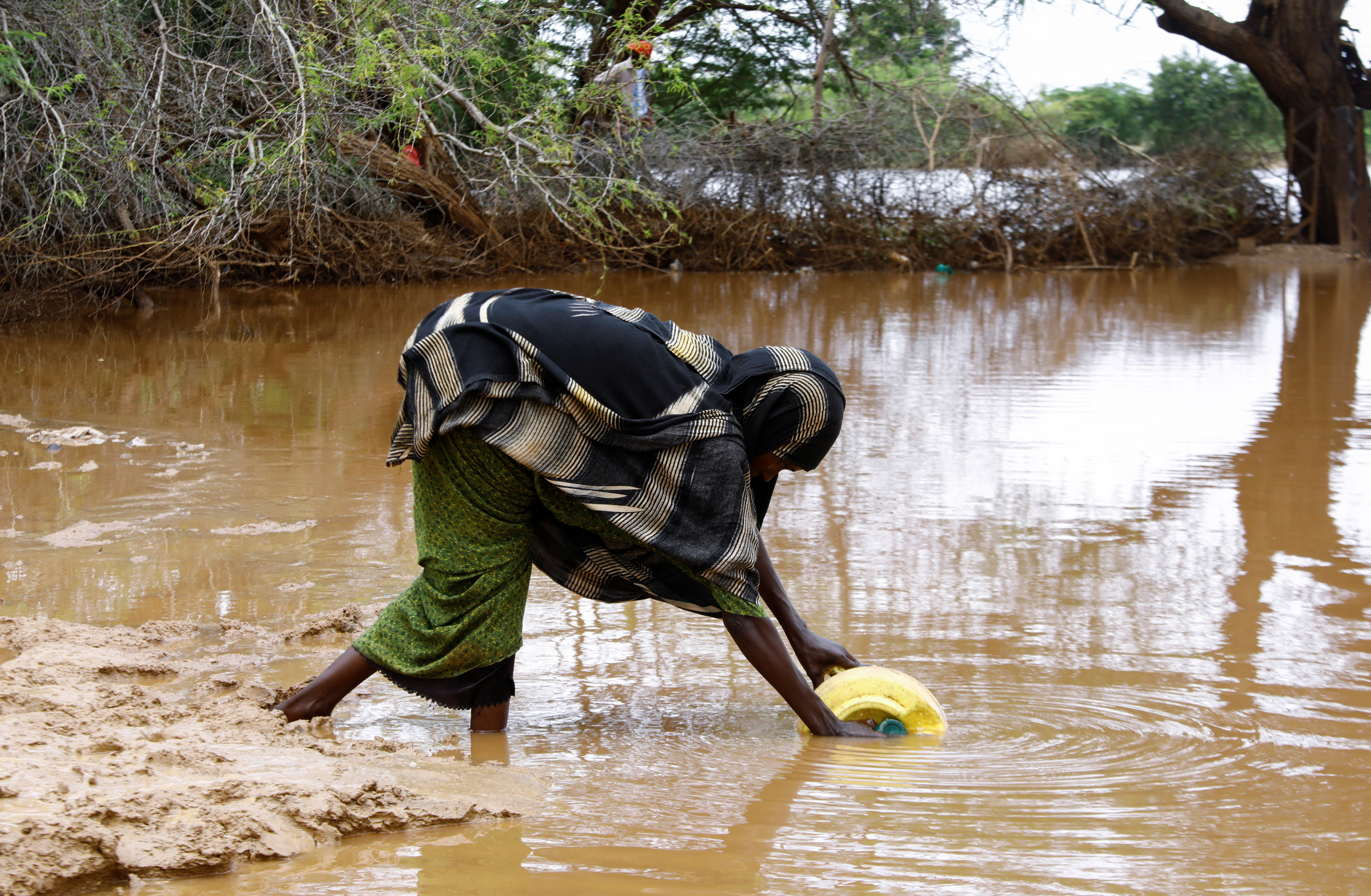 A woman collects flood water following heavy rains that have led the Juba river to overflow and flood large swathes of land in Dolow, Somalia