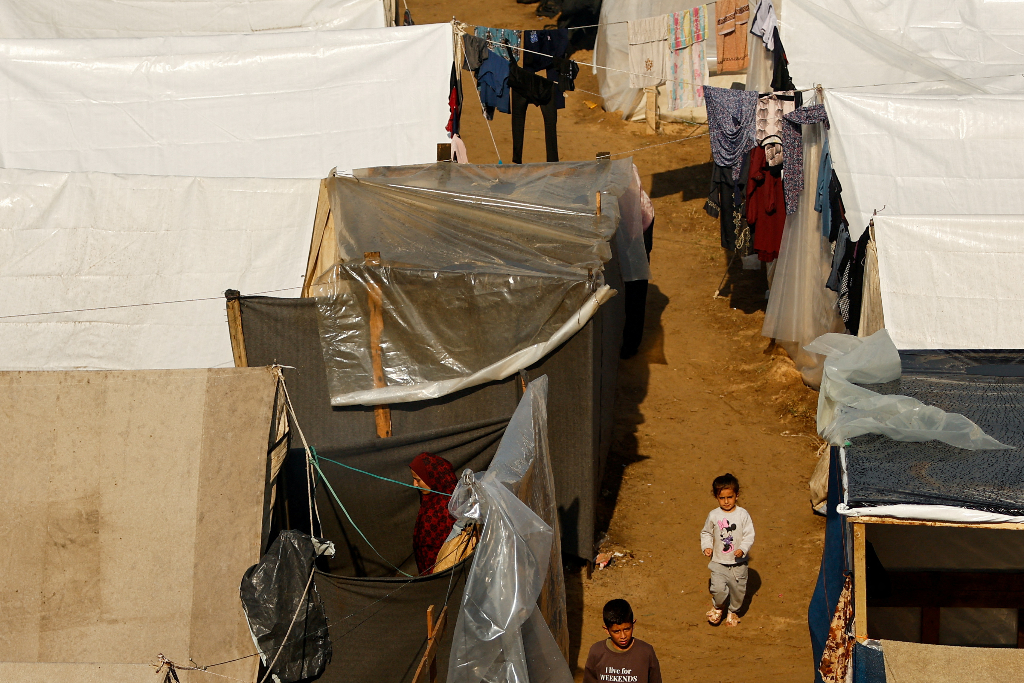 Children walk at a tent camp sheltering displaced Palestinians, amid the ongoing conflict between Israel and Palestinian Islamist group Hamas, following a rainfall, in Khan Younis in the southern Gaza Strip