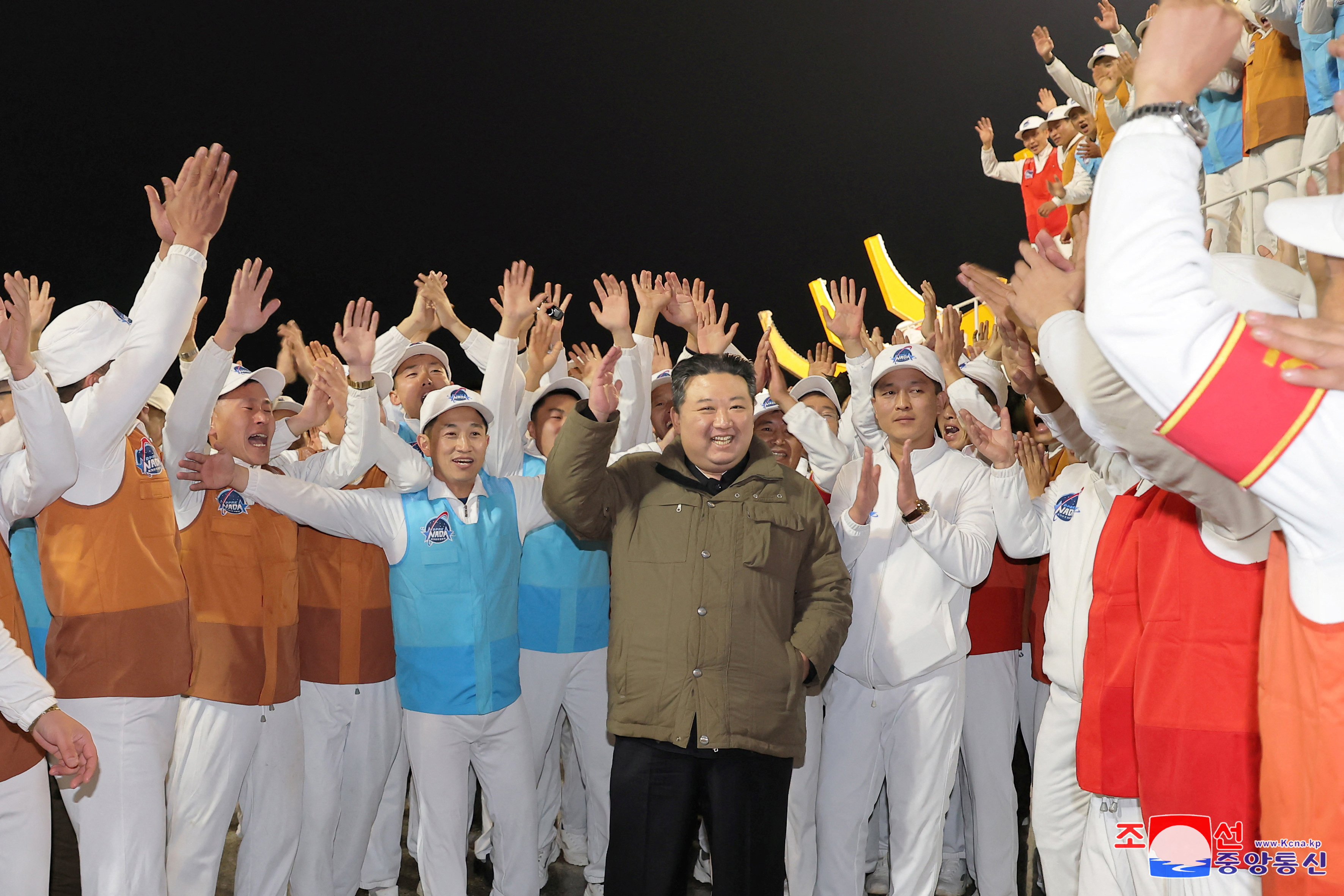 Kim Jong Un celebrating the launch of the spy satellite Malligyong-1. He is smiling and people around him are clapping.
