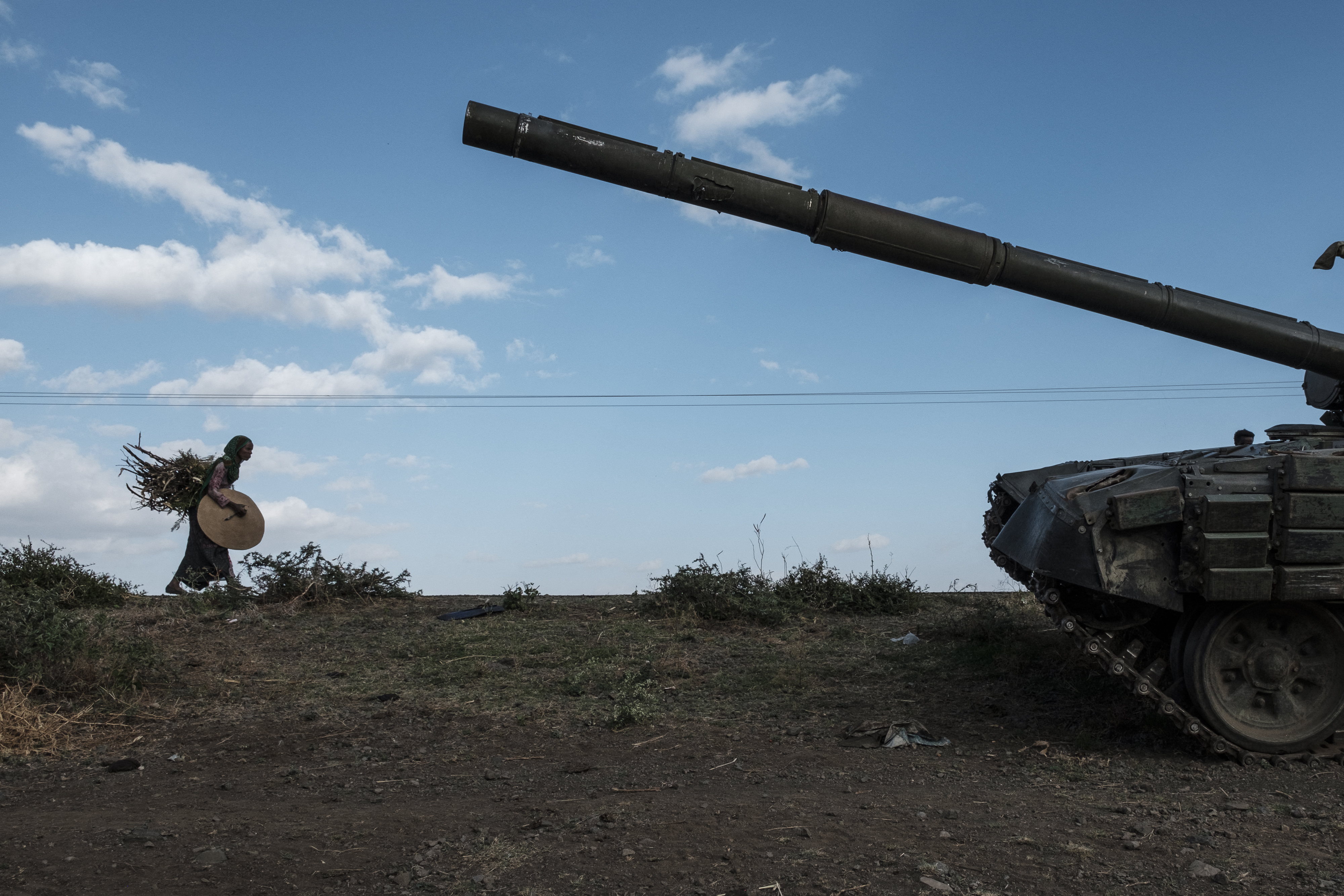 A woman carrying crops walks next to an abandoned tank belonging to Tigrayan forces south of the town of Mehoni, Ethiopia.