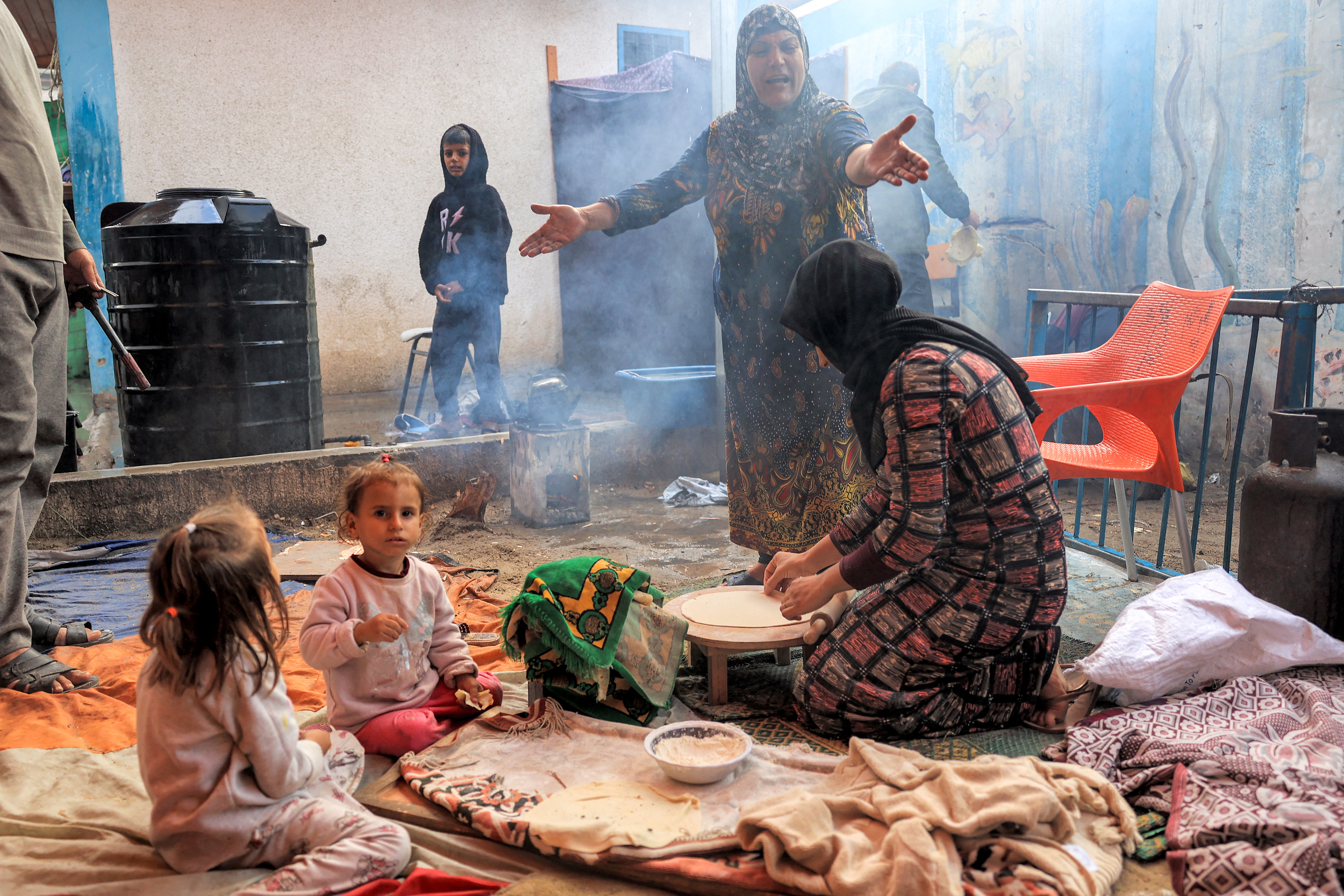 A woman reacts while another prepares traditional unleavened bread on an open fire at school run by the United Nations Relief and Works Agency for Palestine Refugees in the Near East (UNRWA) in Rafah in the southern Gaza Strip.