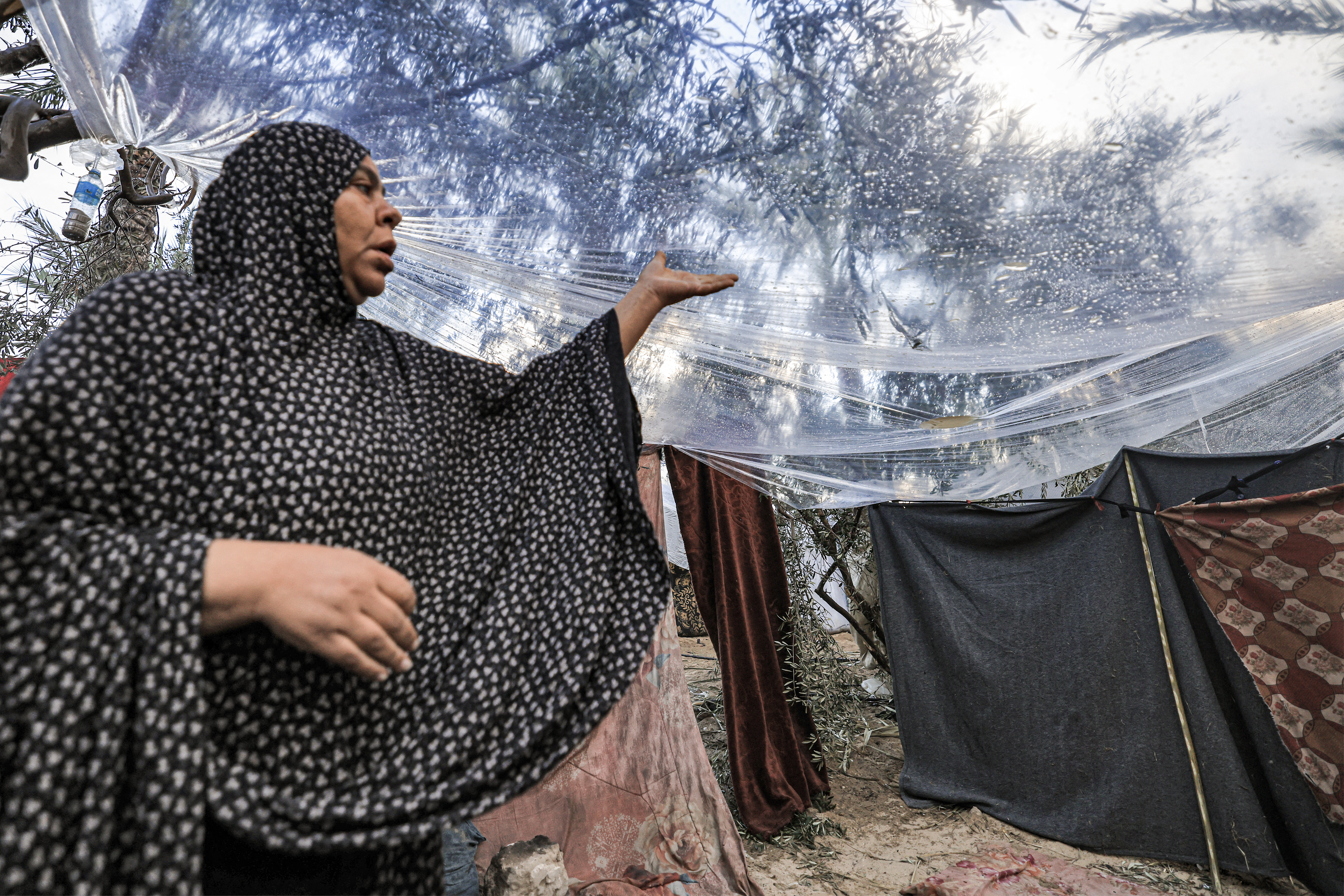 A woman stands under a plastic sheet spread to protect from rain in the area outside tents pitched by Palestinians taking shelter from Israeli bombardment around Nasser Hospital, in Khan Yunis in the southern Gaza Strip on November 14