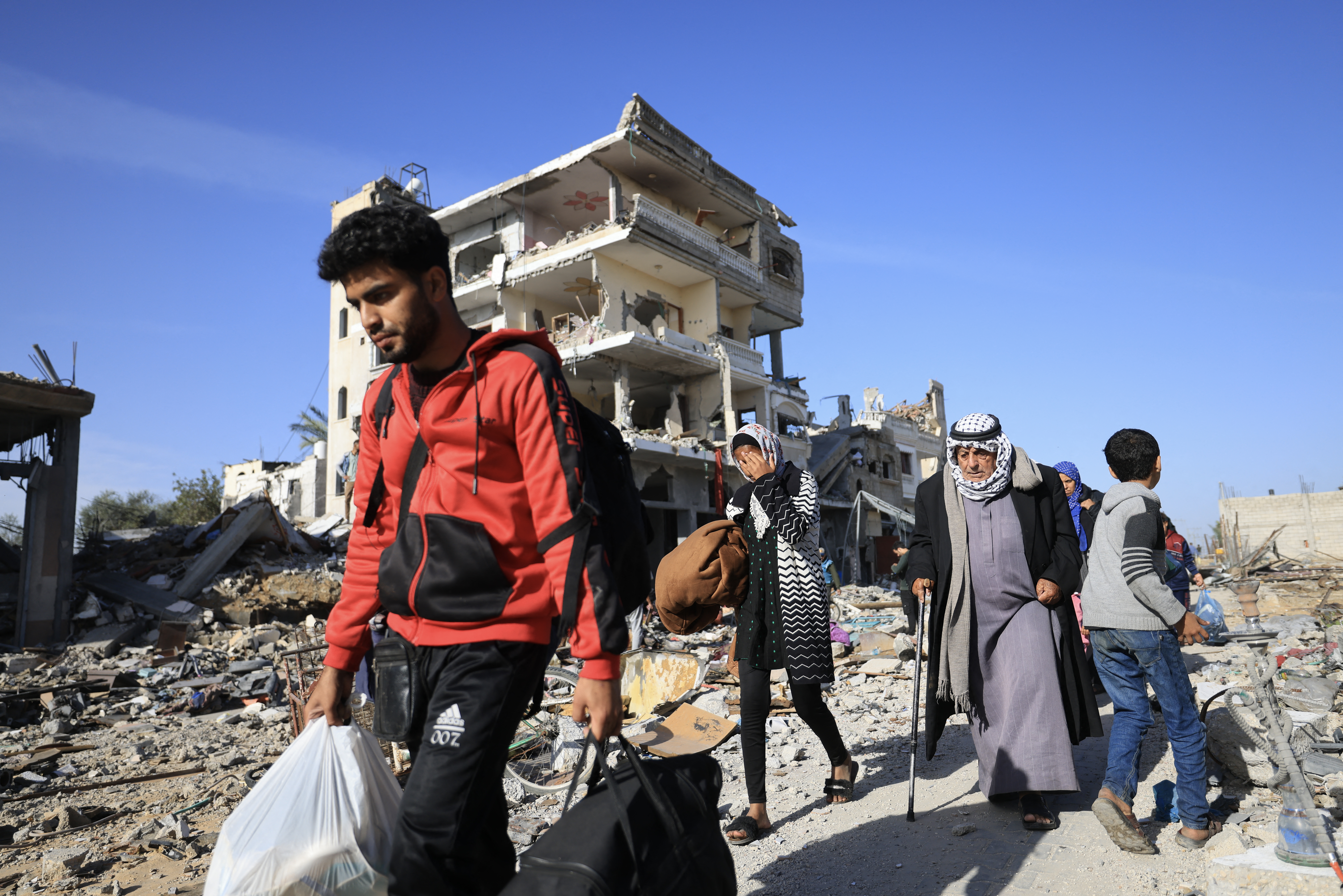 Palestinians walk through debris upon their return to Khan Yunis to inspect their homes following weeks of Israeli bombardment, in the Khezaa district on the eastern outskirts of the southern Gaza Strip city on November 24