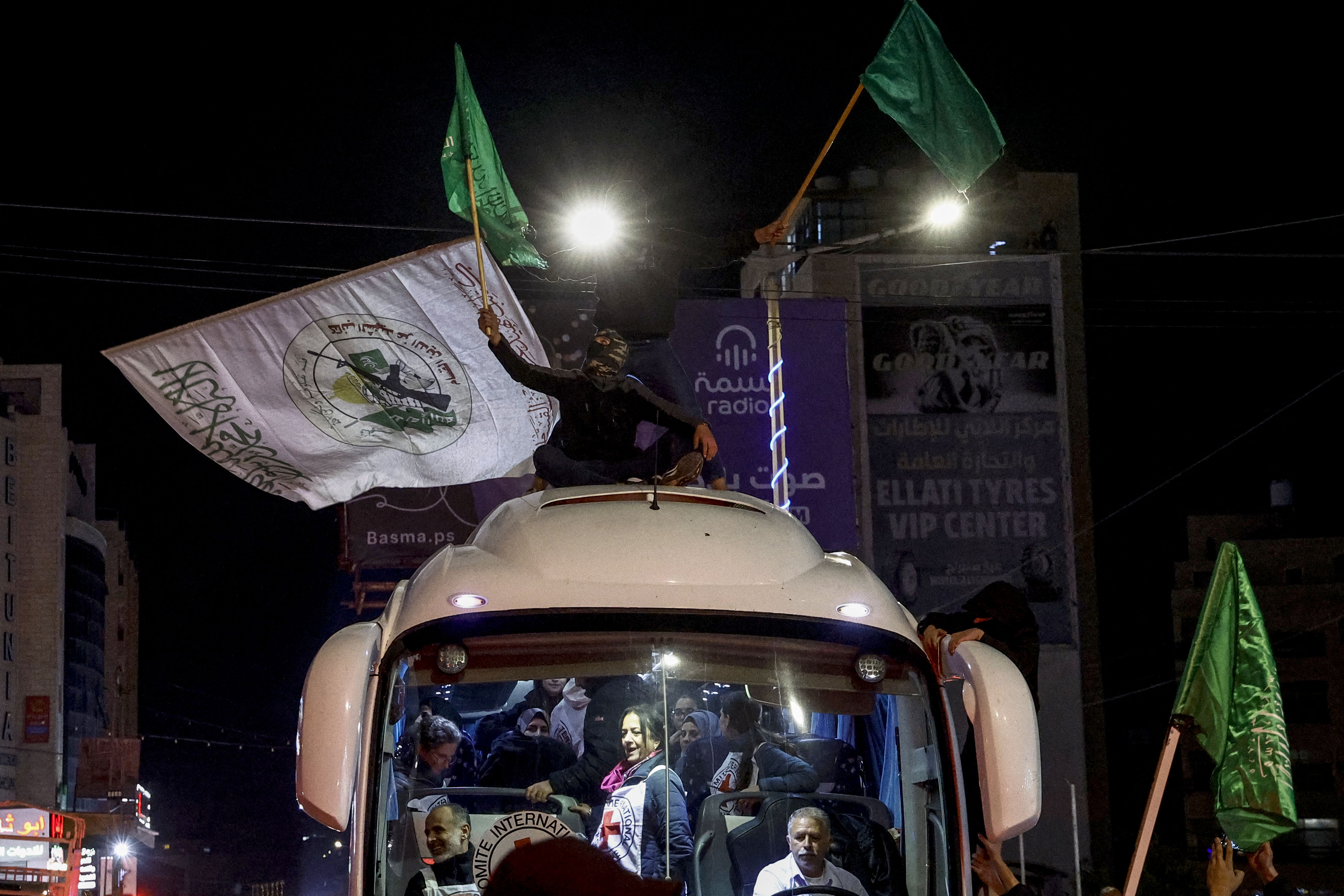Men wave the Hamas flag as a crowd surrounds a Red Cross bus carrying Palestinian prisoners released from Israeli jails in exchange for hostages released by Hamas from the Gaza Strip, in Ramallah in the occupied West Bank.