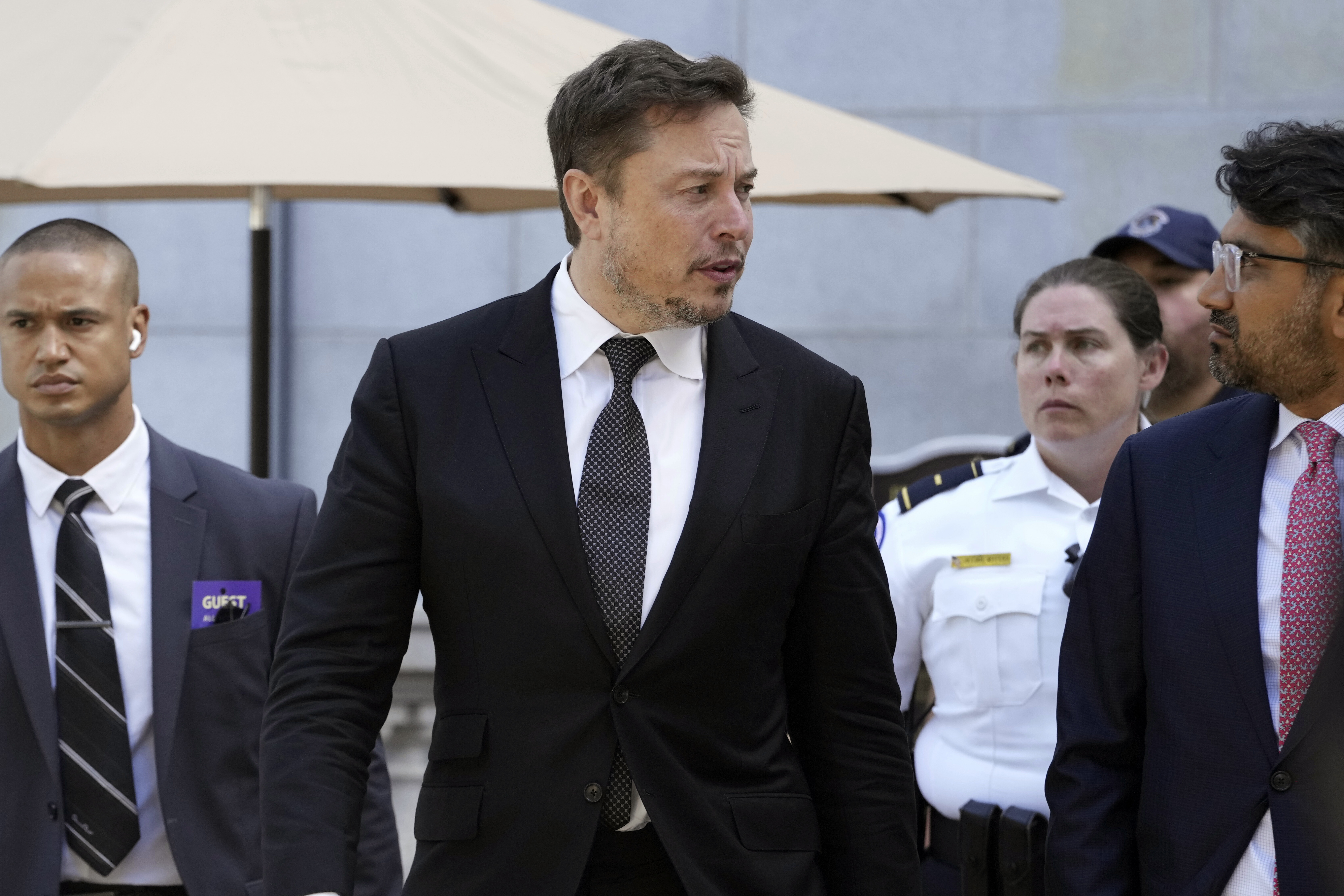 Elon Musk in suit walking with other people