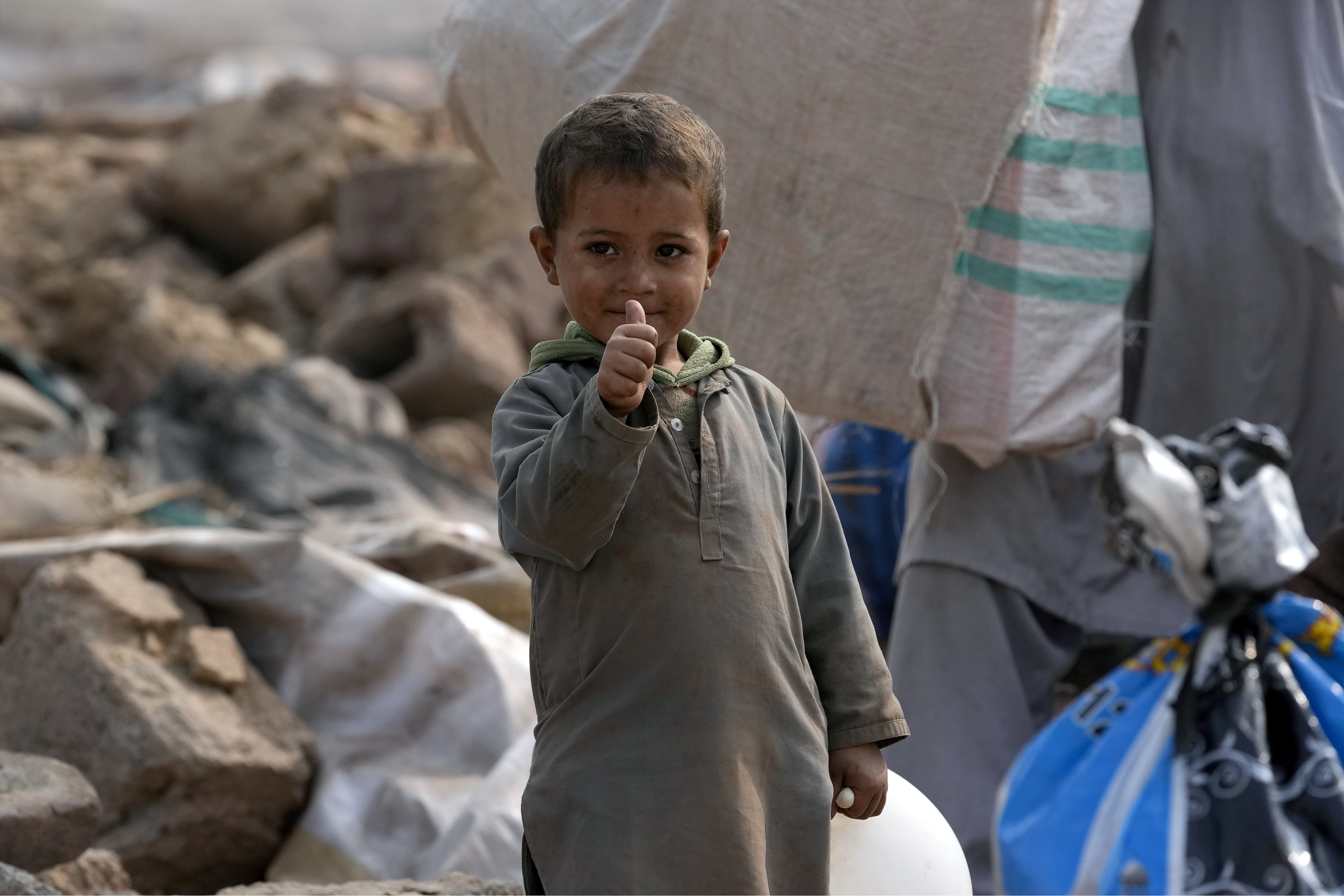 An Afghan boy gestures as he stands beside his family's belongings retrieved from their damage mud homes demolished by authorities during a crackdown against an illegal settlement and immigrants, on the outskirts of Islamabad, Pakistan.