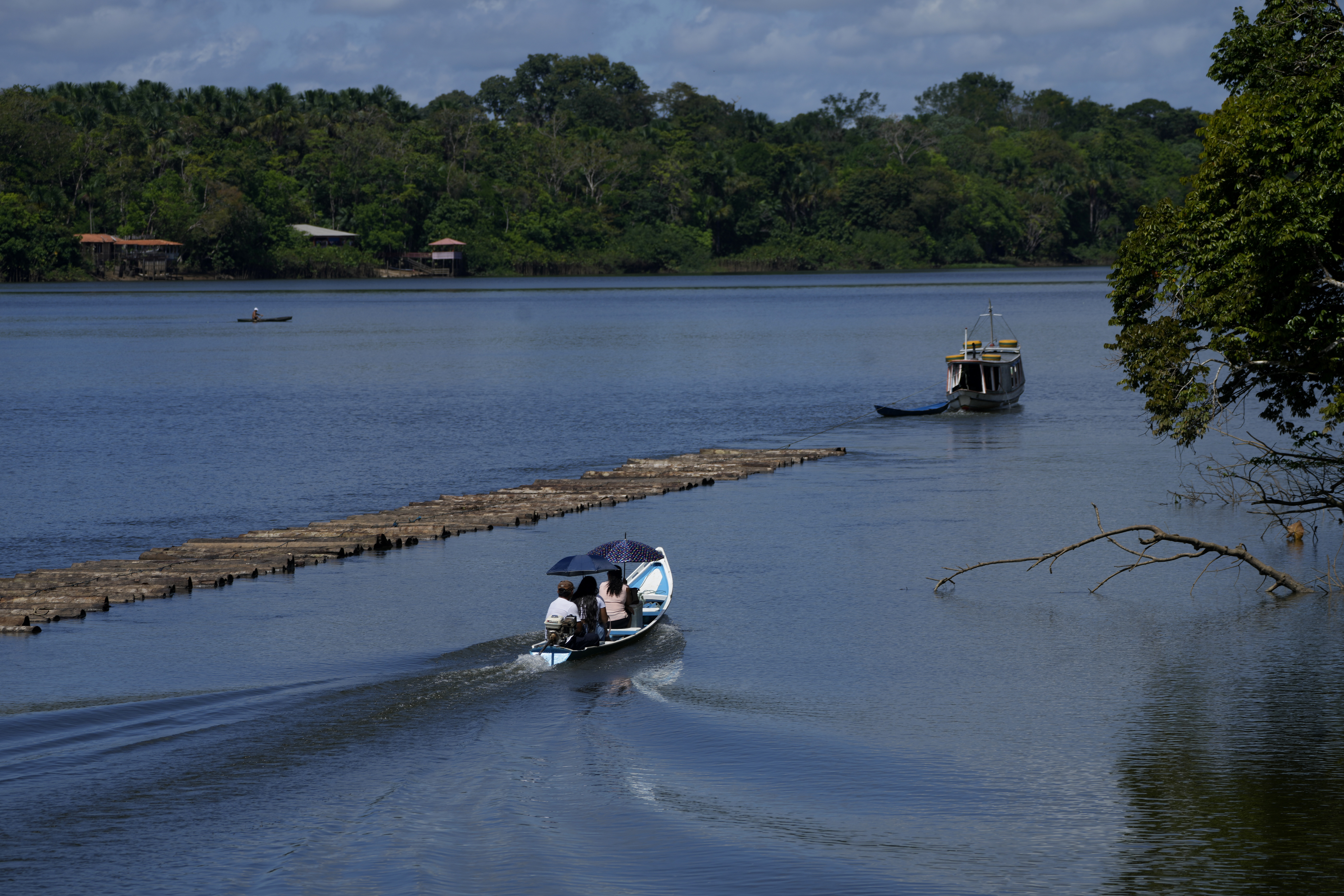 A family travels in a boat shaded by umbrellas next to a boat transporting wooden logs in a section of the Tocantis River, next the island of Tauare, in the municipality of Mocajuba, Para state, Brazil.