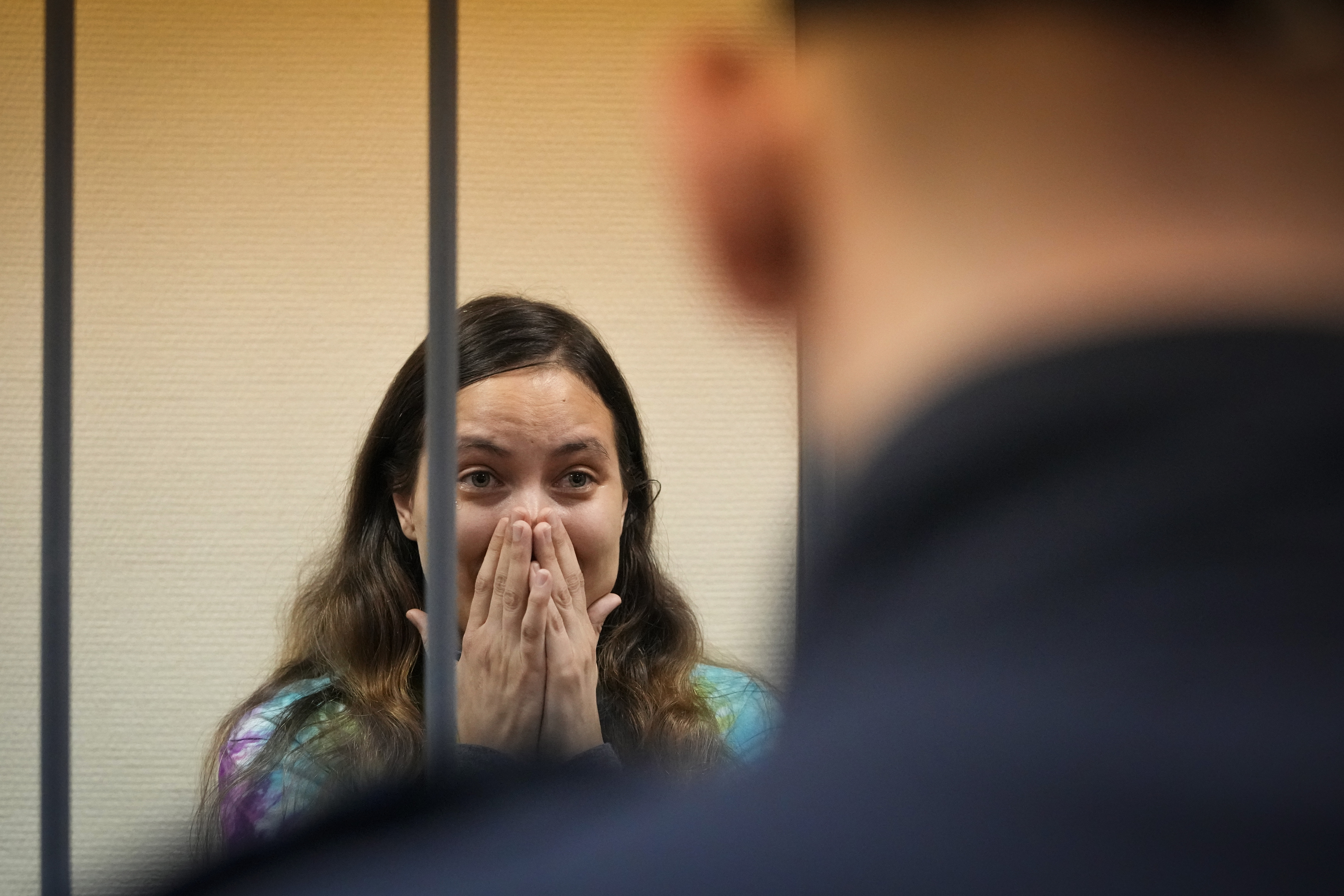Sasha Skochilenko reacts the verdict. She is standing in the dock and has her hands to ger face covering her nose and mouth A police officer is in front.