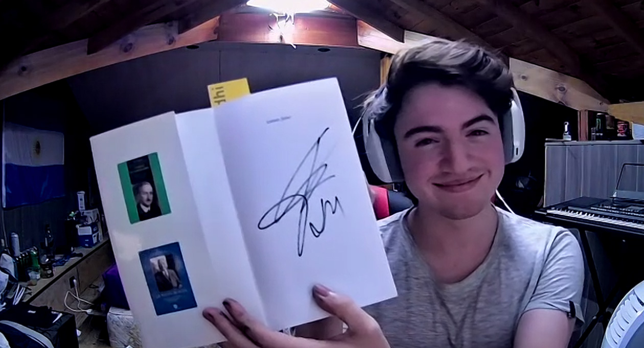 A screenshot of a young man wearing headphones and holding up a text book signed by Javier Milei.
