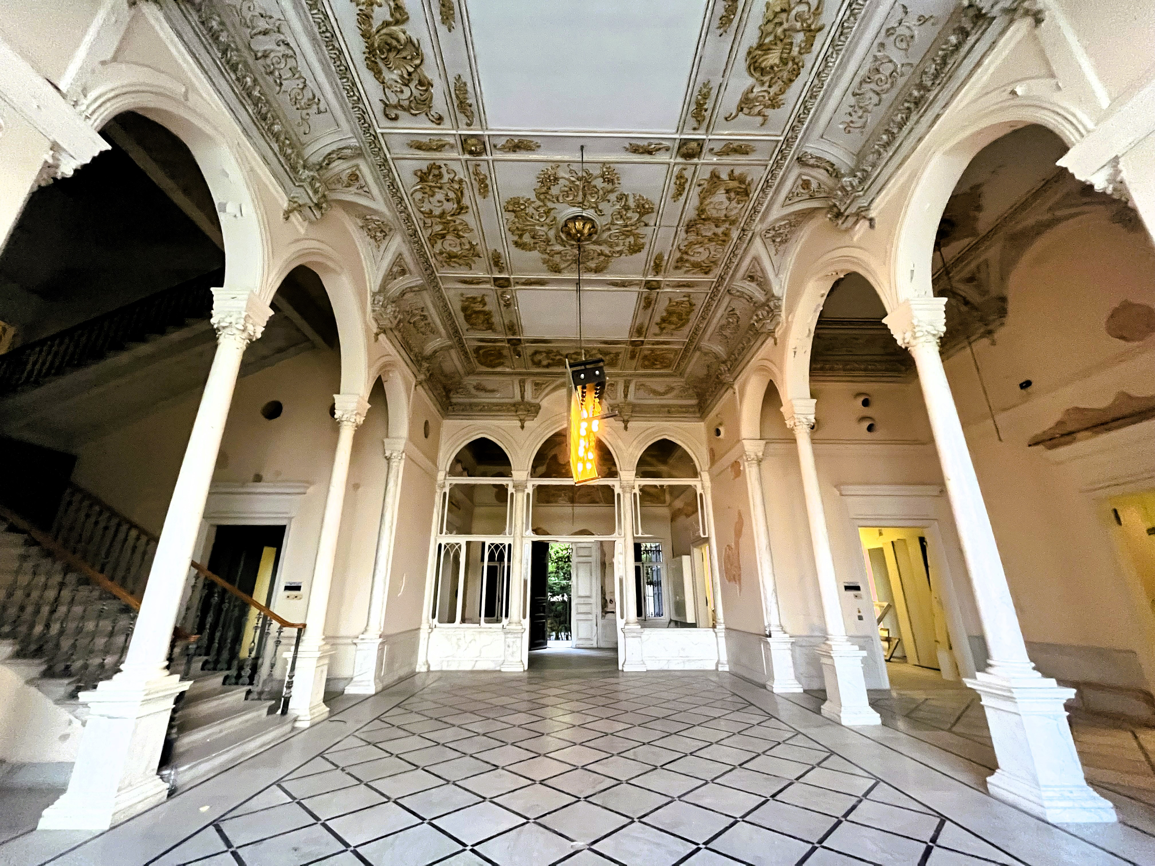 Wide view of the corridor with the grey gilt ceiling, white arched arcades to either side