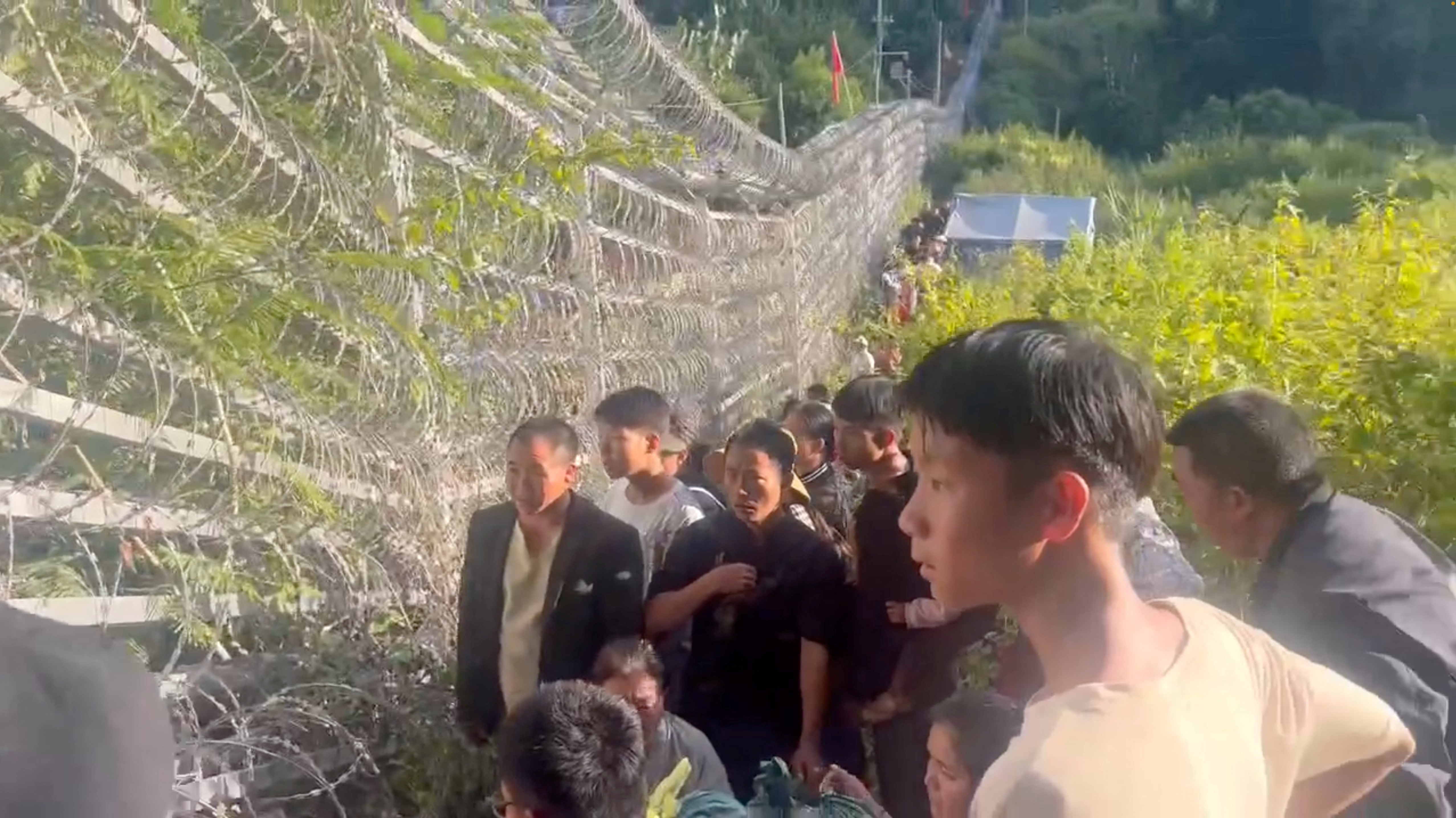 People crowding at the border fence between Myanmar and China. It is tall and covered in razor wire