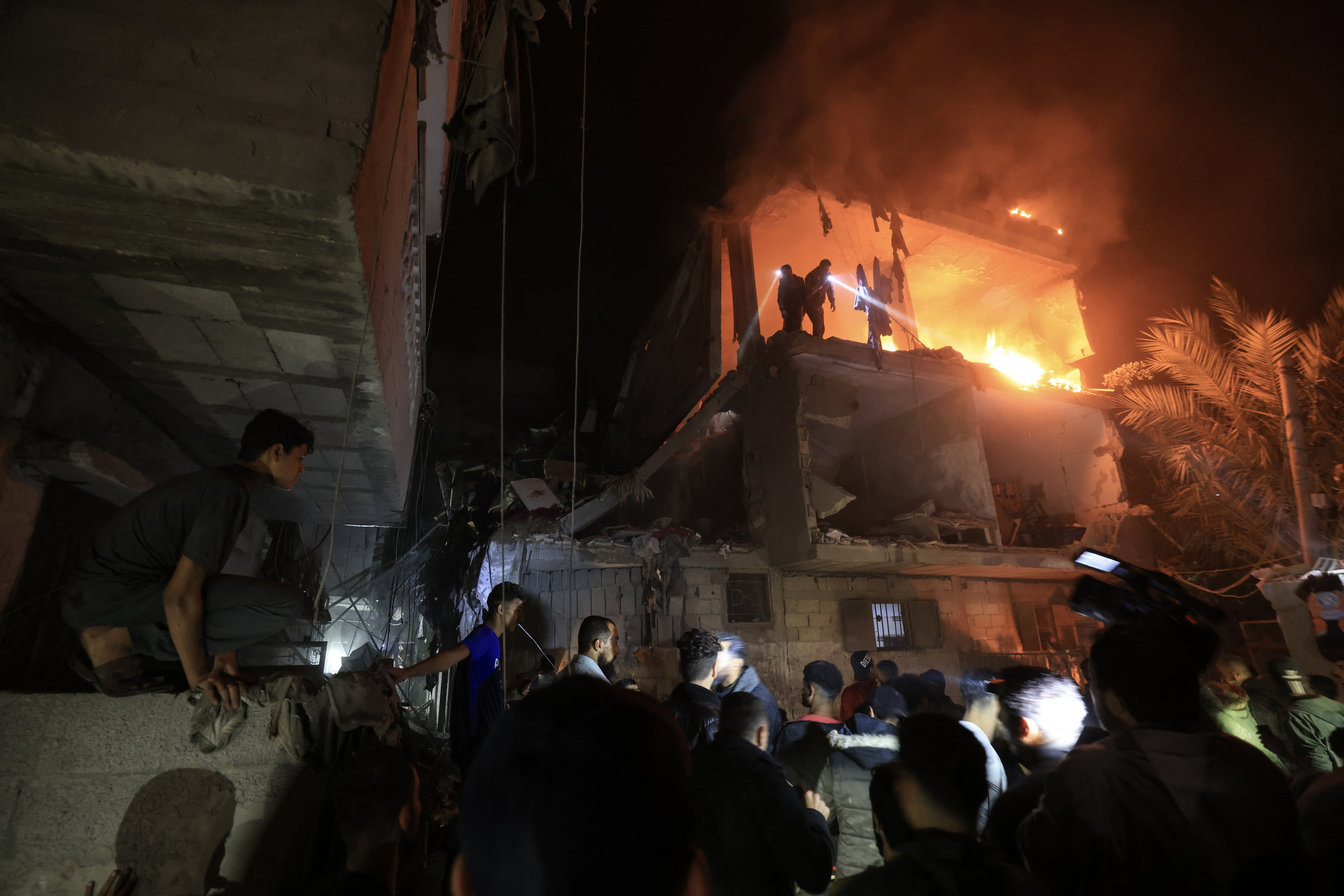 People use the lights on their telephones to search for victims amid the rubble of a smouldering building, following an Israeli strike in Rafah in the southern Gaza Strip.