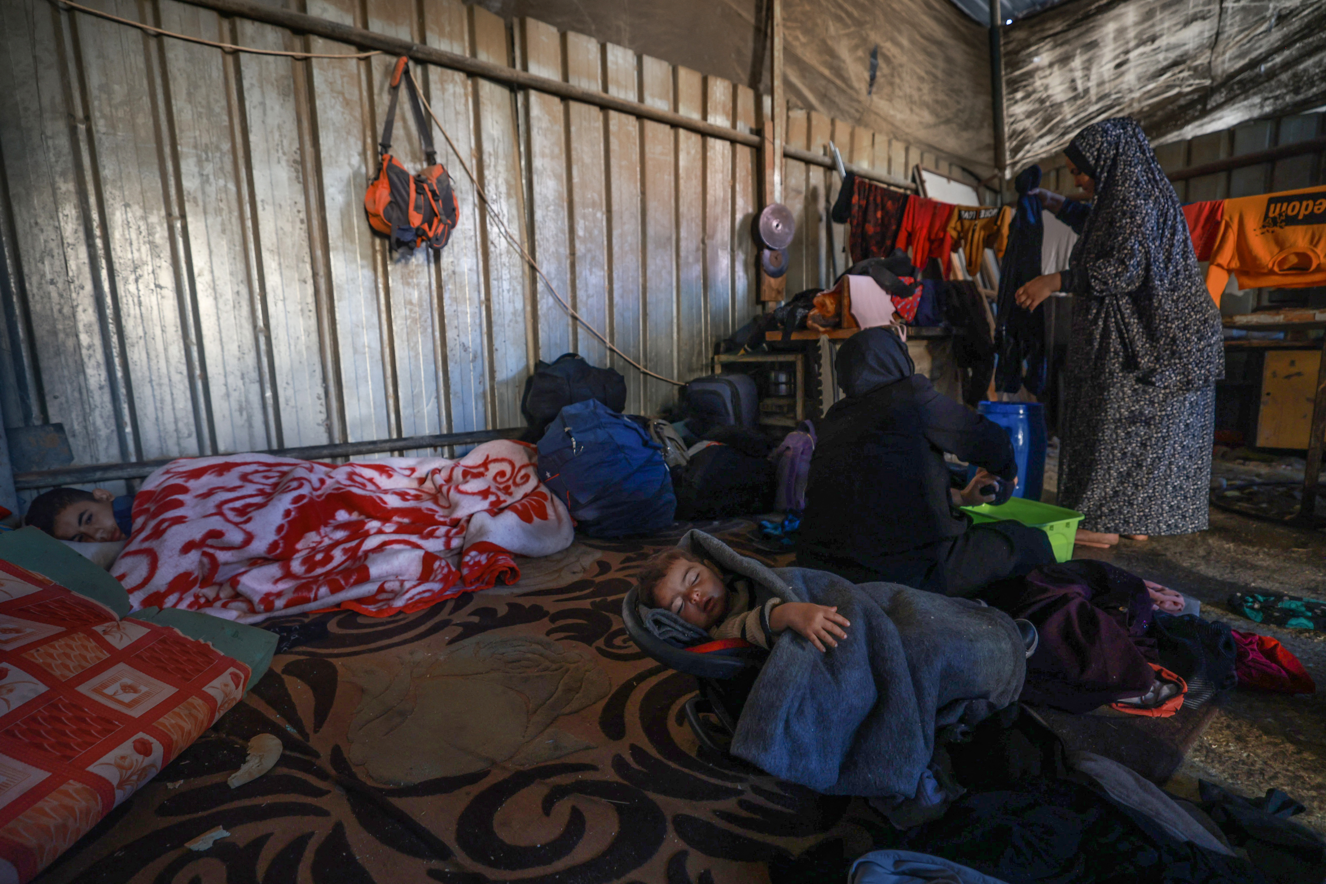 Members of a Palestinian family who fled Gaza City to Khan Yunis and had to recently flee to Rafah in the southern Gaza Strip, cook as children sleep, inside a workshop where they found temporary shelter, on December 9