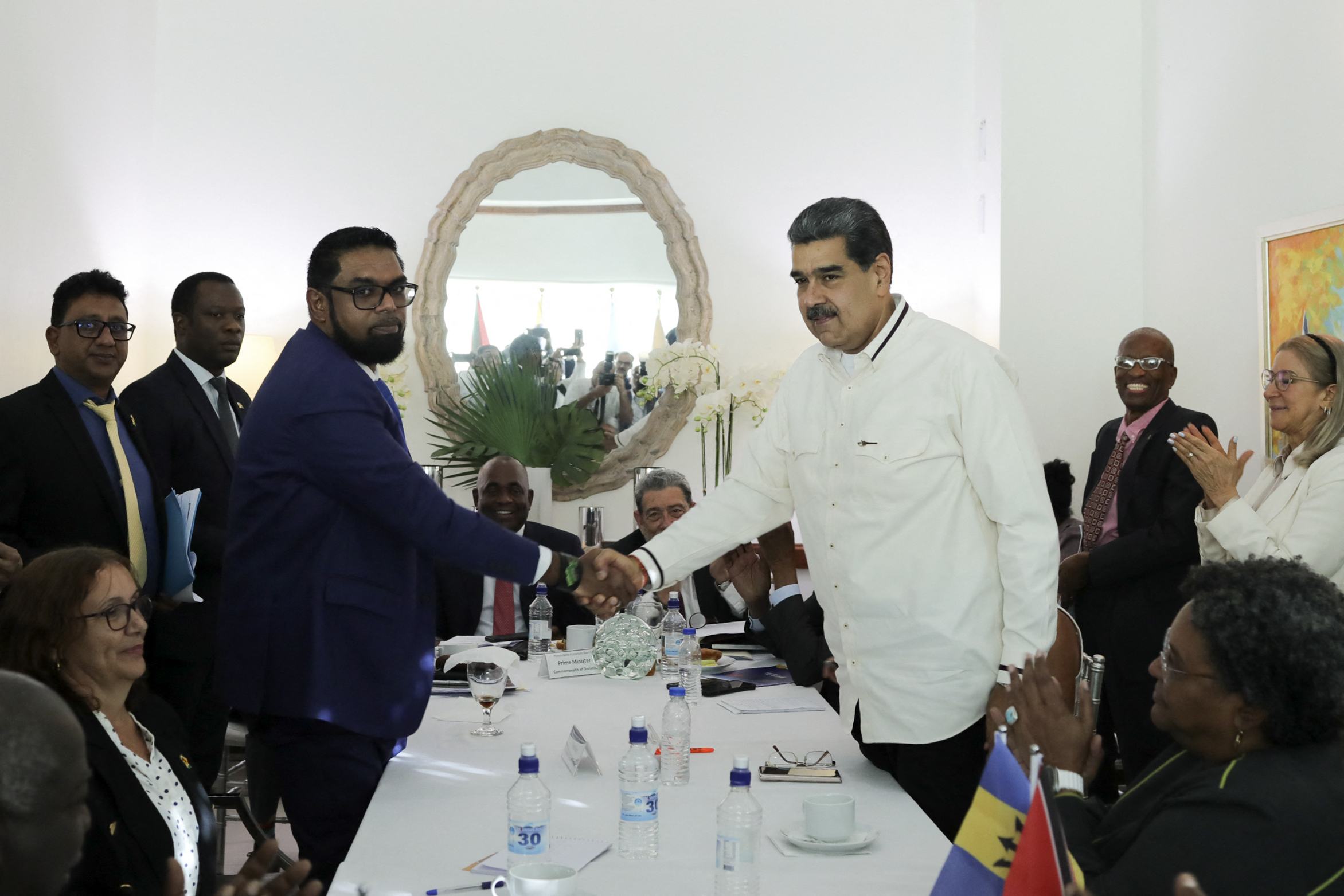 Nicolas Maduro and Irfaan Ali shake hands across a table. They look tense. Aides are sitting around them.
