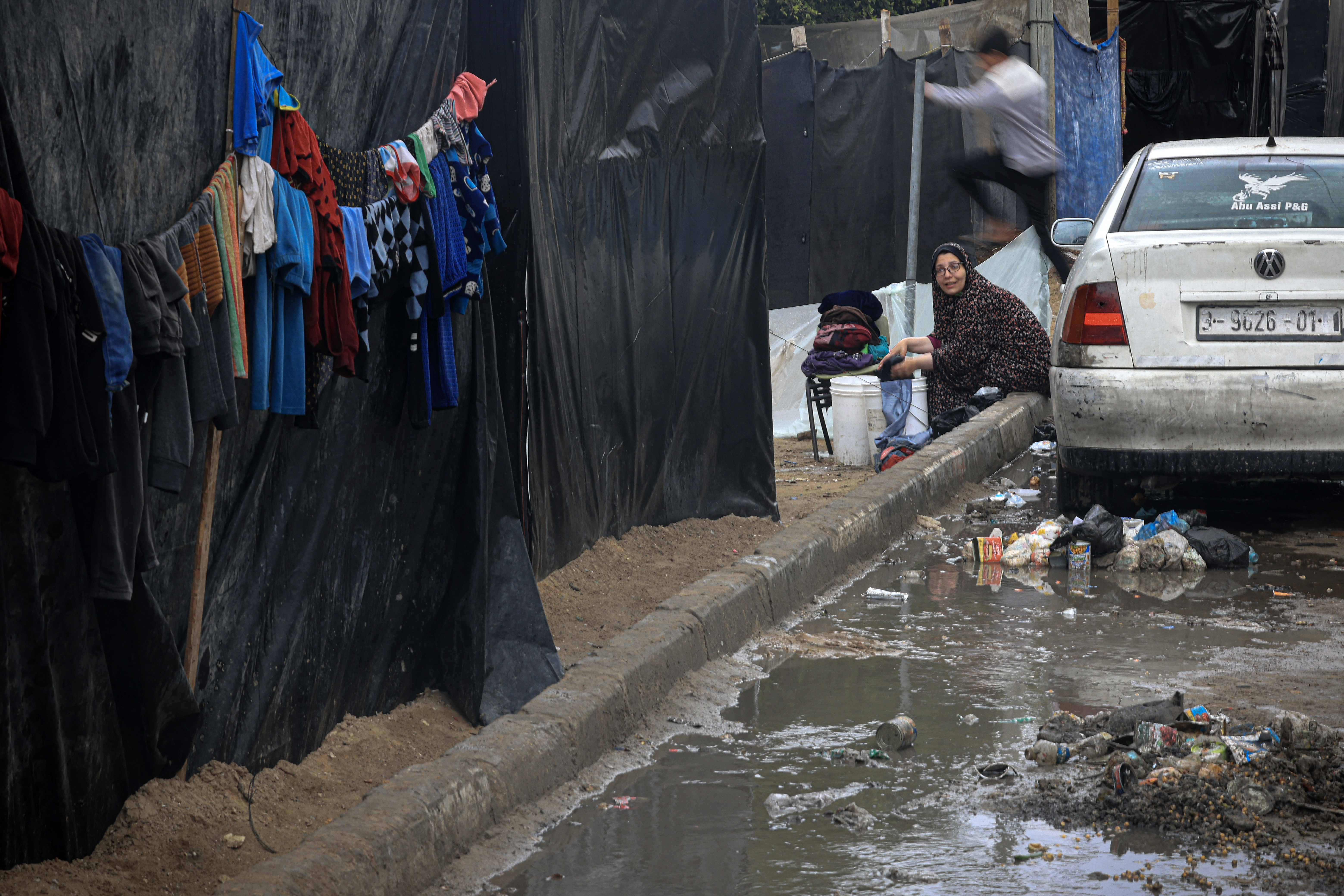 A Palestinian woman washes clothes along a flooded street at camp for displaced people in Rafah, in the southern Gaza Strip, where most civilians have taken refuge as battles continue between Israel and the Palestinian militant group Hamas.