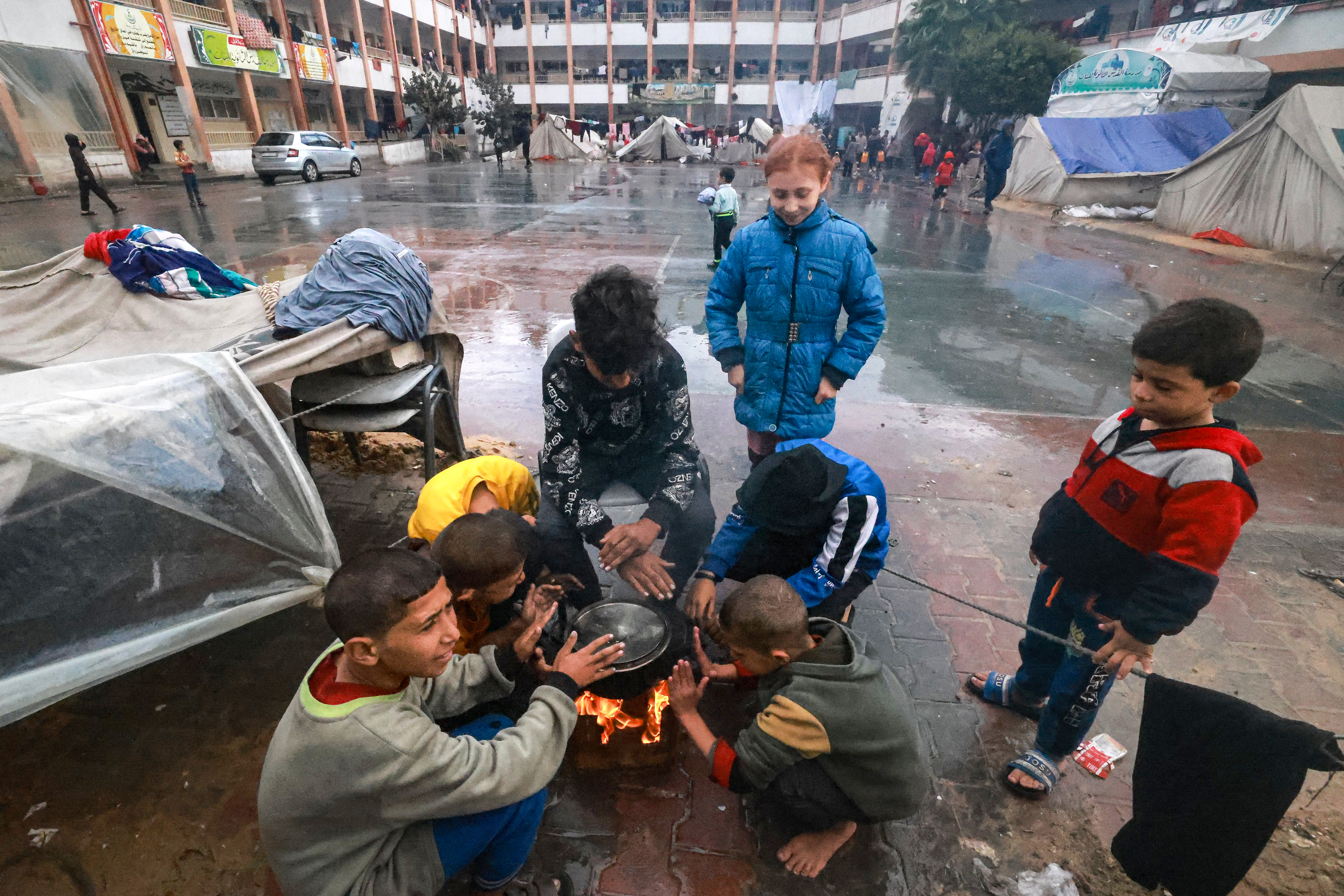 Palestinians children warm up around a fire outside their makeshift tent at a camp set up on a schoolyard in Rafah in the southern Gaza Strip where most civilians have taken refuge.