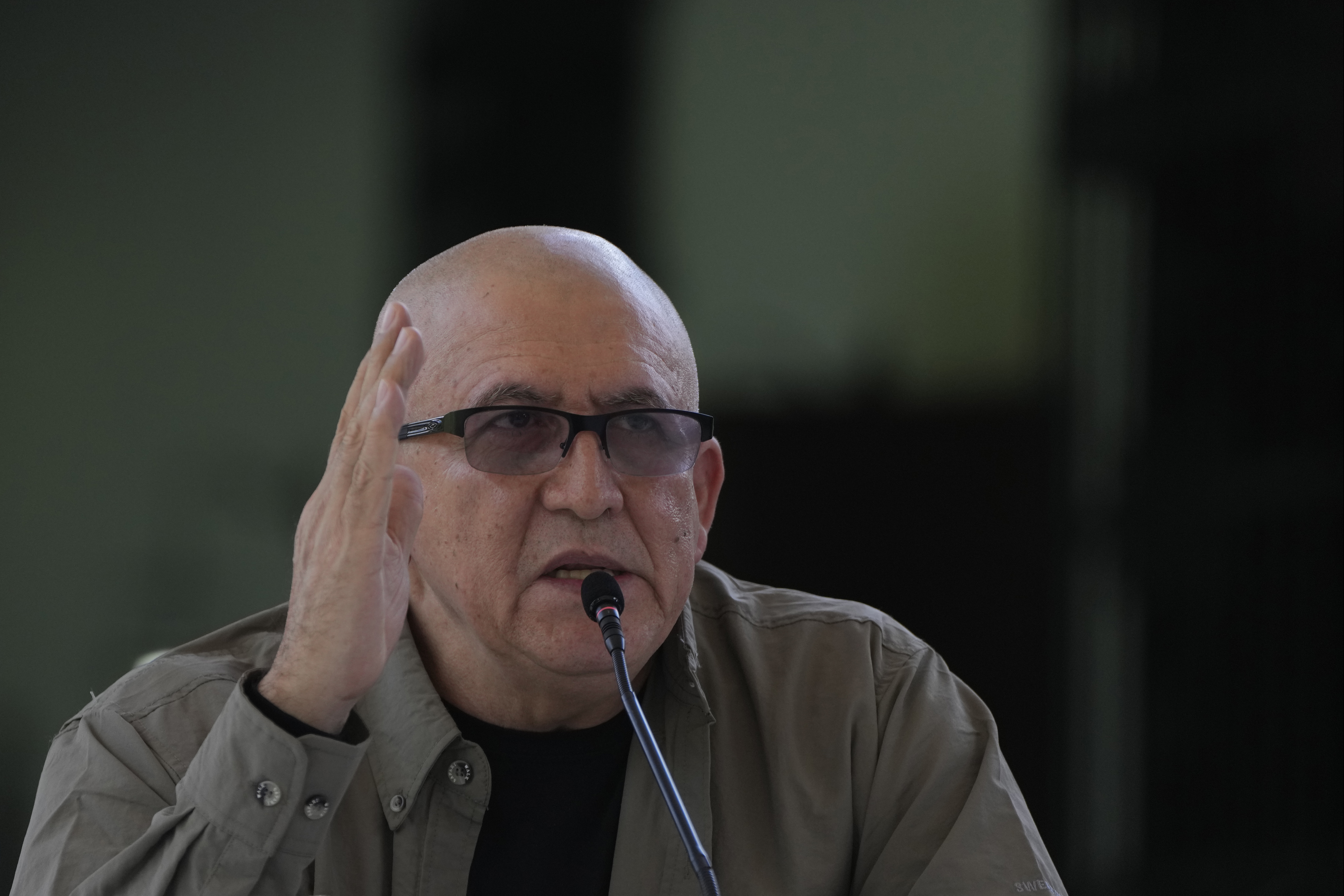 Antonio Garcia, a bald man with dark-rimmed glasses and an olive-colored shirt, gestures with his hands as he speaks into a microphone.