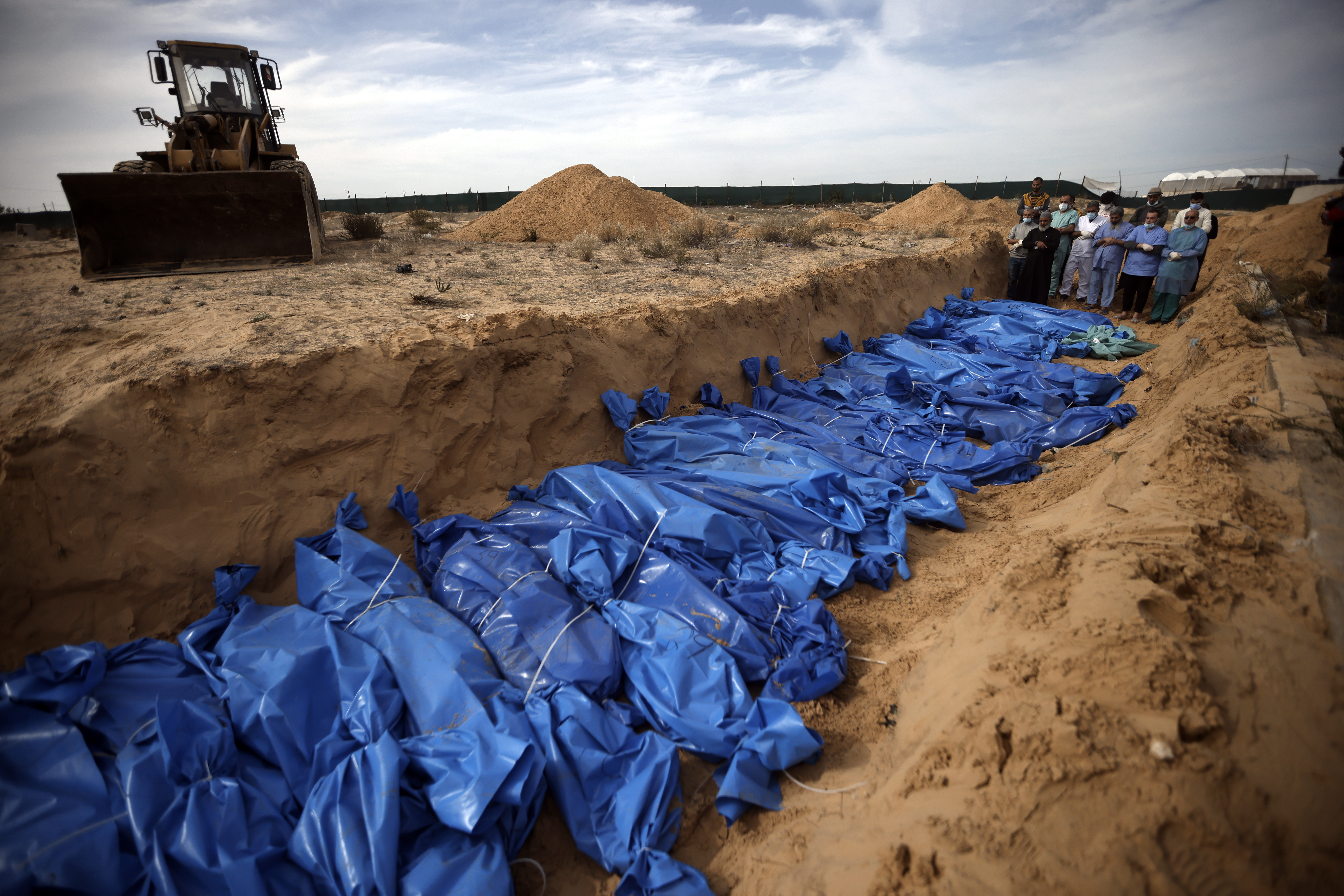 Palestinians pray over bodies of people killed in the Israeli bombardment who were brought from the Shifa hospital before burying them in a mass grave in the town of Khan Younis