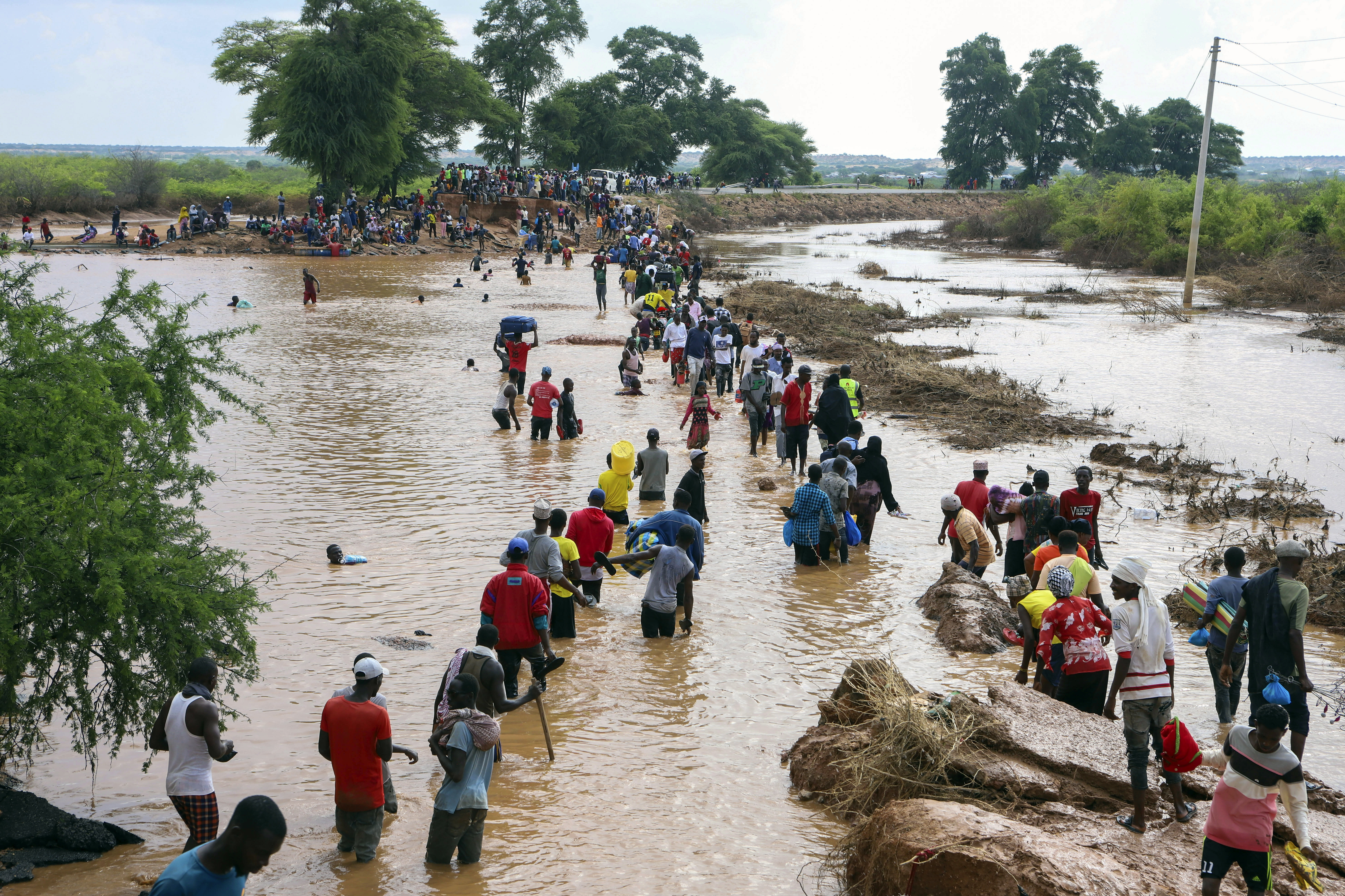 People wade over flood waters after a section of road was destroyed by floods at Mororo, border of Tana River and Garissa, North Eastern Kenya.