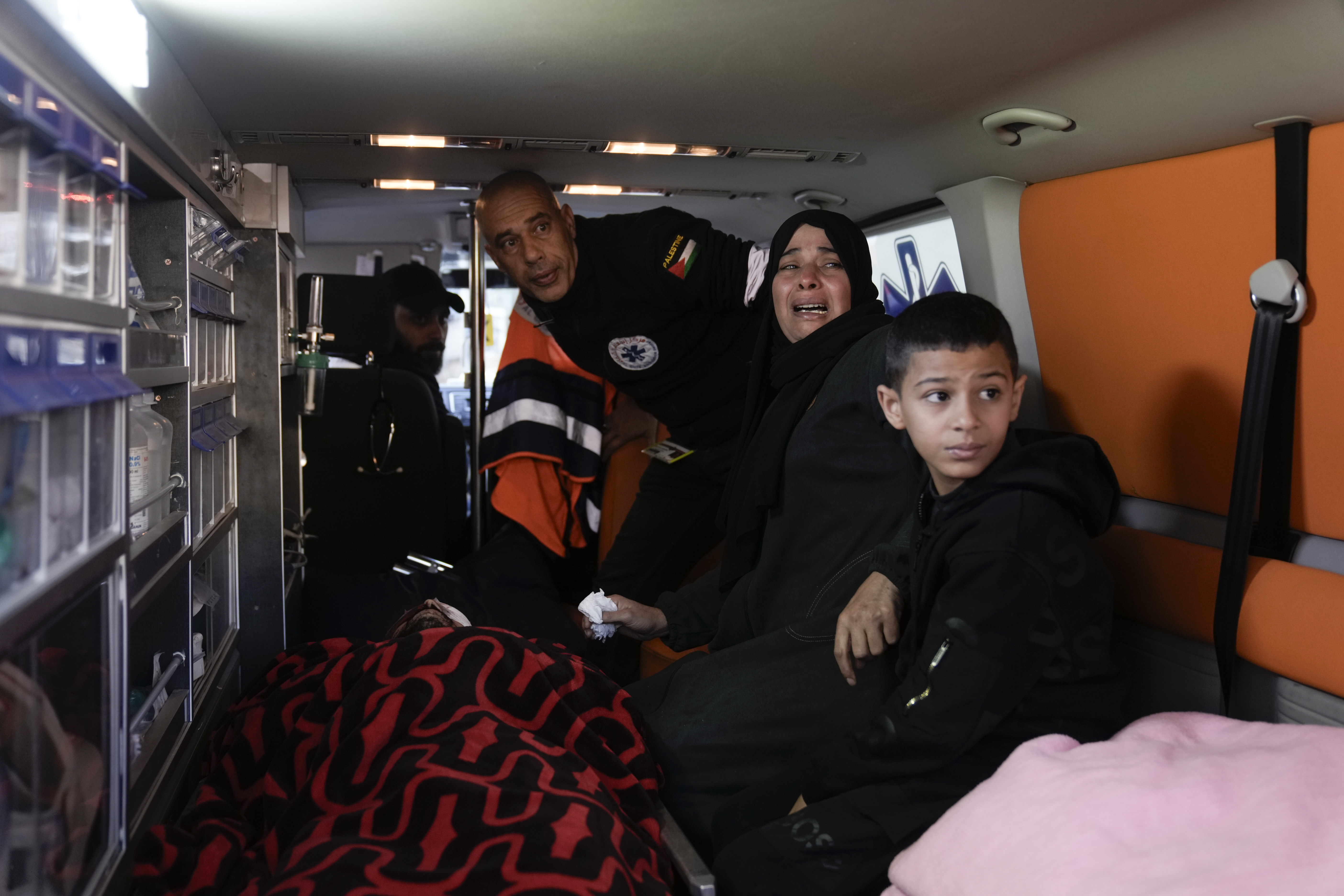 Palestinians sit by a relative killed during an Israeli military raid on Nur Shams refugee camp in the West Bank on Sunday, Dec. 17