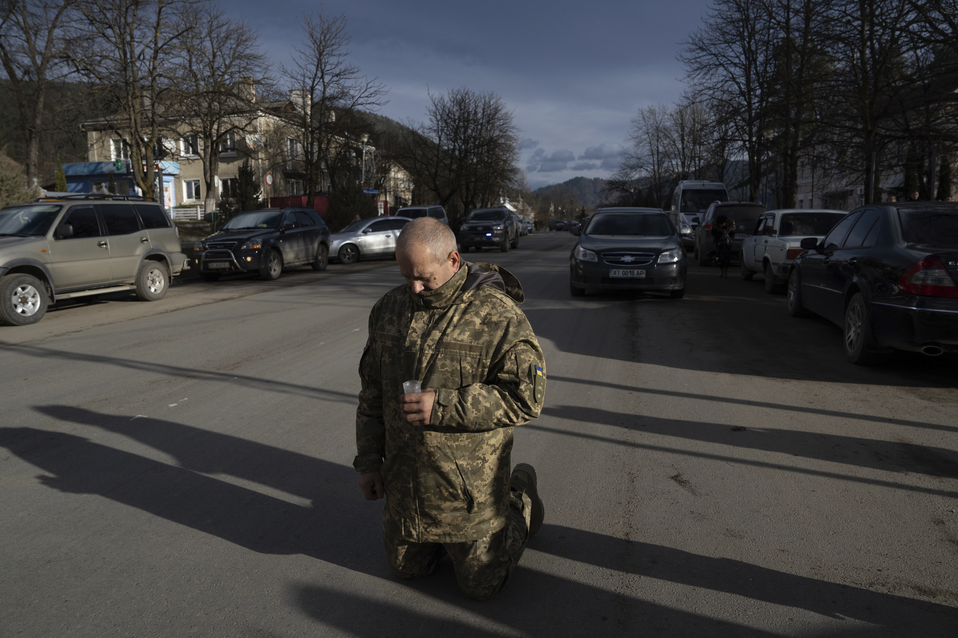 A Ukrainian soldier kneeling in the street to pay his respects to a fallen comrade
