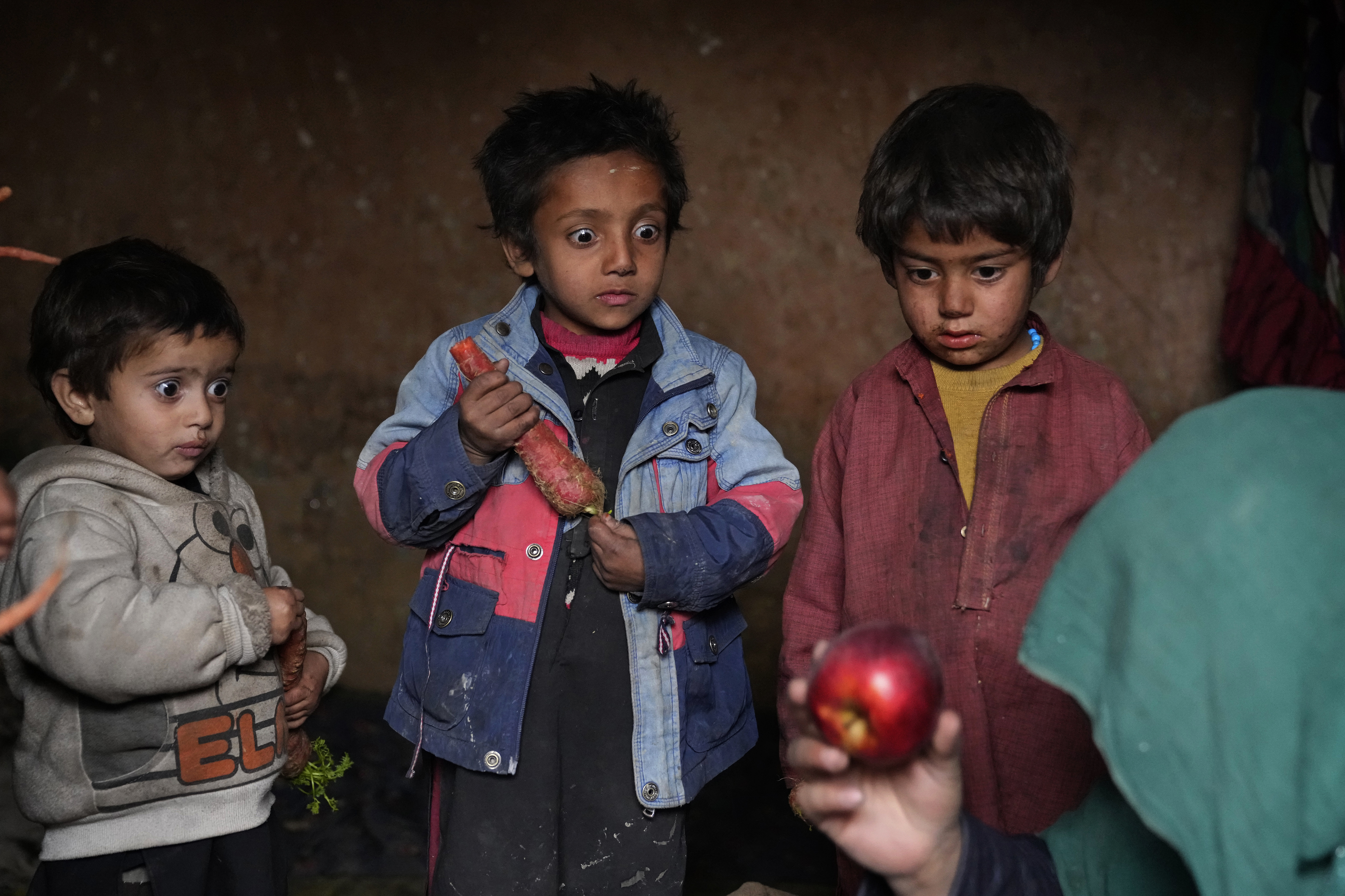 Three internally displaced children look with surprise at an apple that their mother brought home after begging, in a camp on the outskirts of Kabul, Afghanistan, Thursday, Feb 2