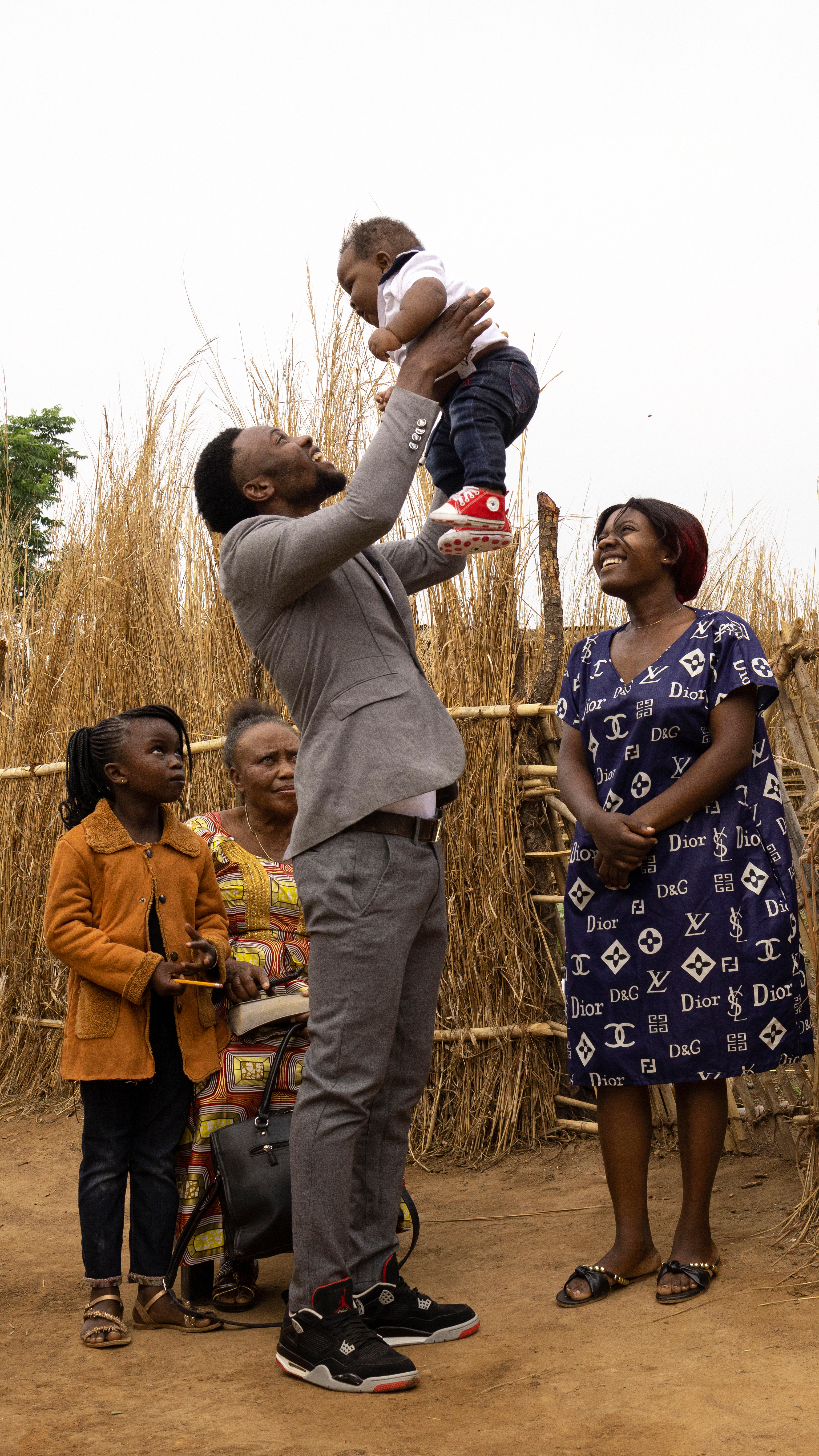A young man smiles holding a baby, as a girl and two women watch