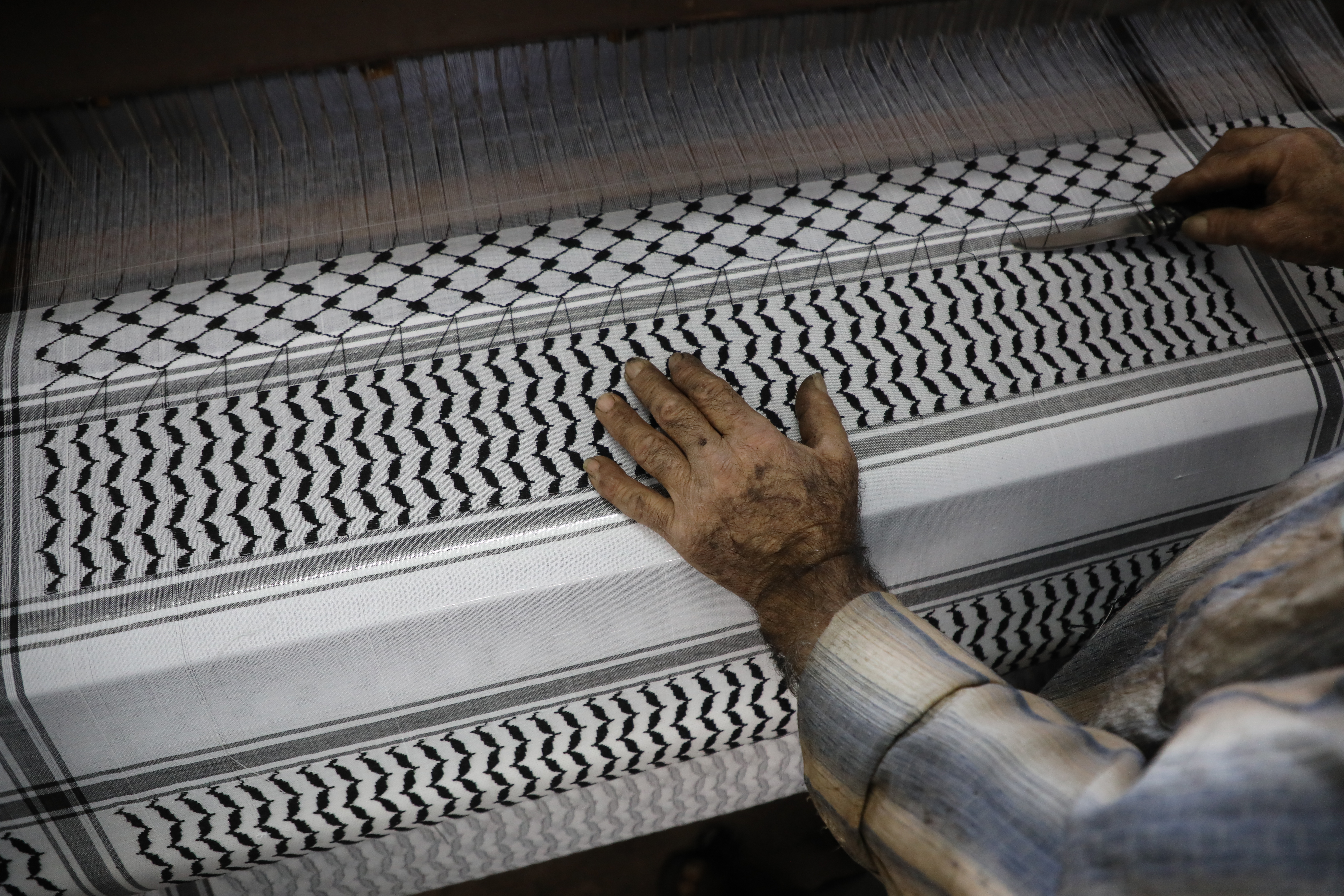 Hand on a roll of keffiyeh fabric coming off loom