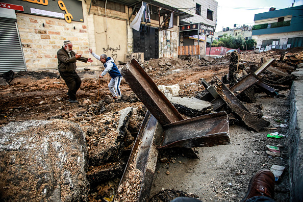 Palestinians walk on a damaged road following an Israeli military raid in Jenin refugee camp.